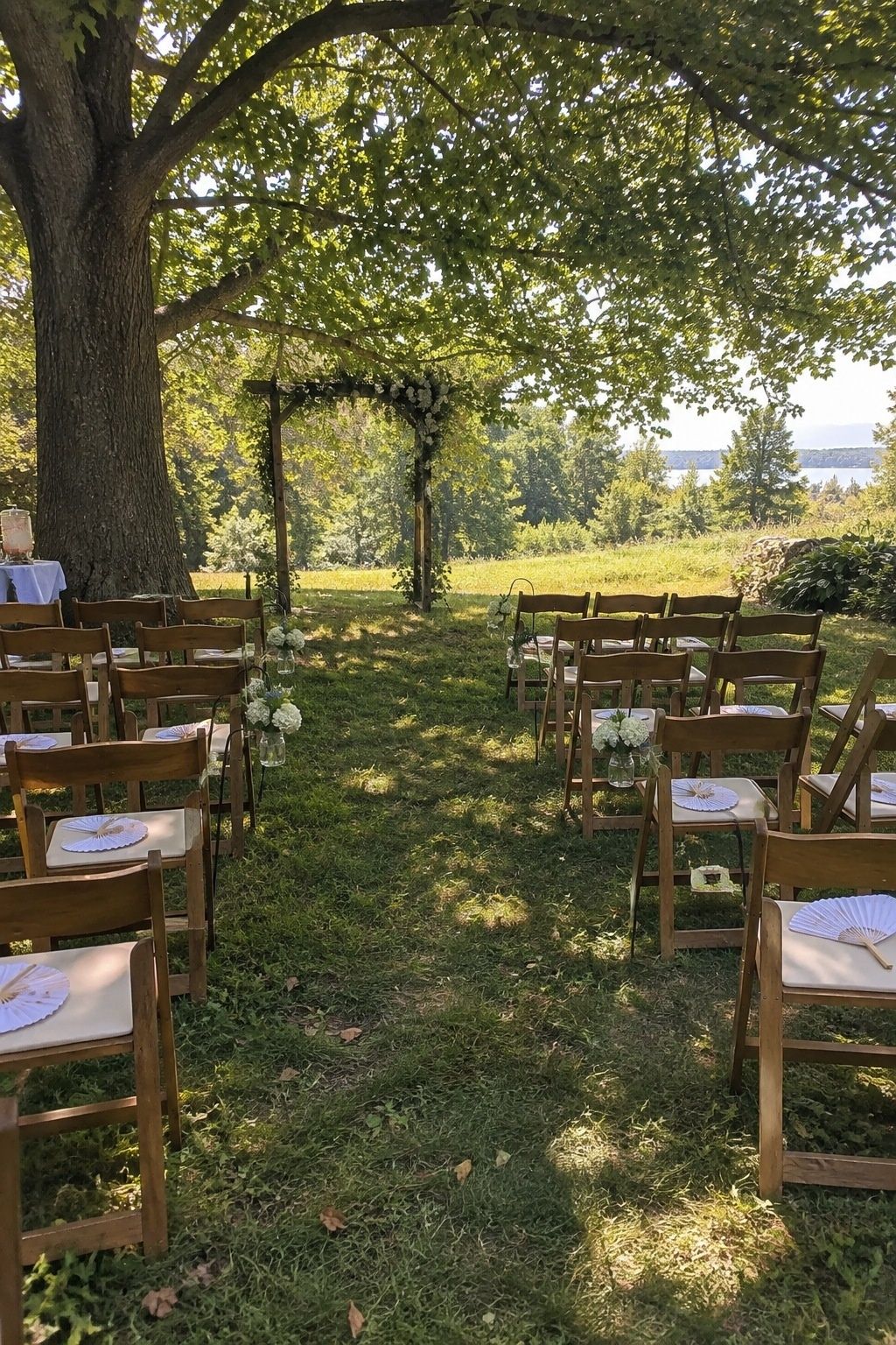 Small outdoor wedding ceremony chairs and fans under tree shade