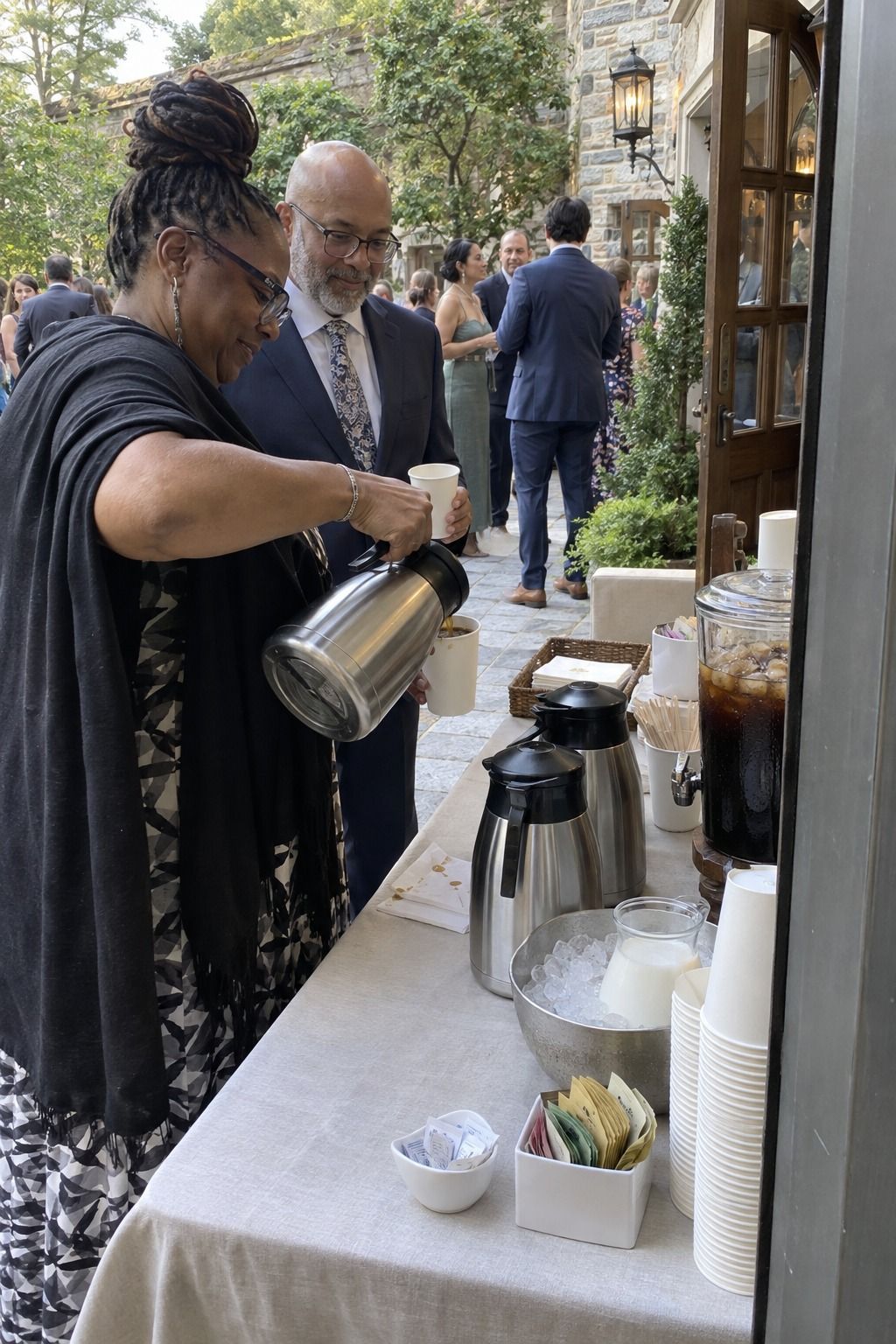 Guests actively use a shaded entrance coffee point with thermal servers, cold brew and milk held on ice.
