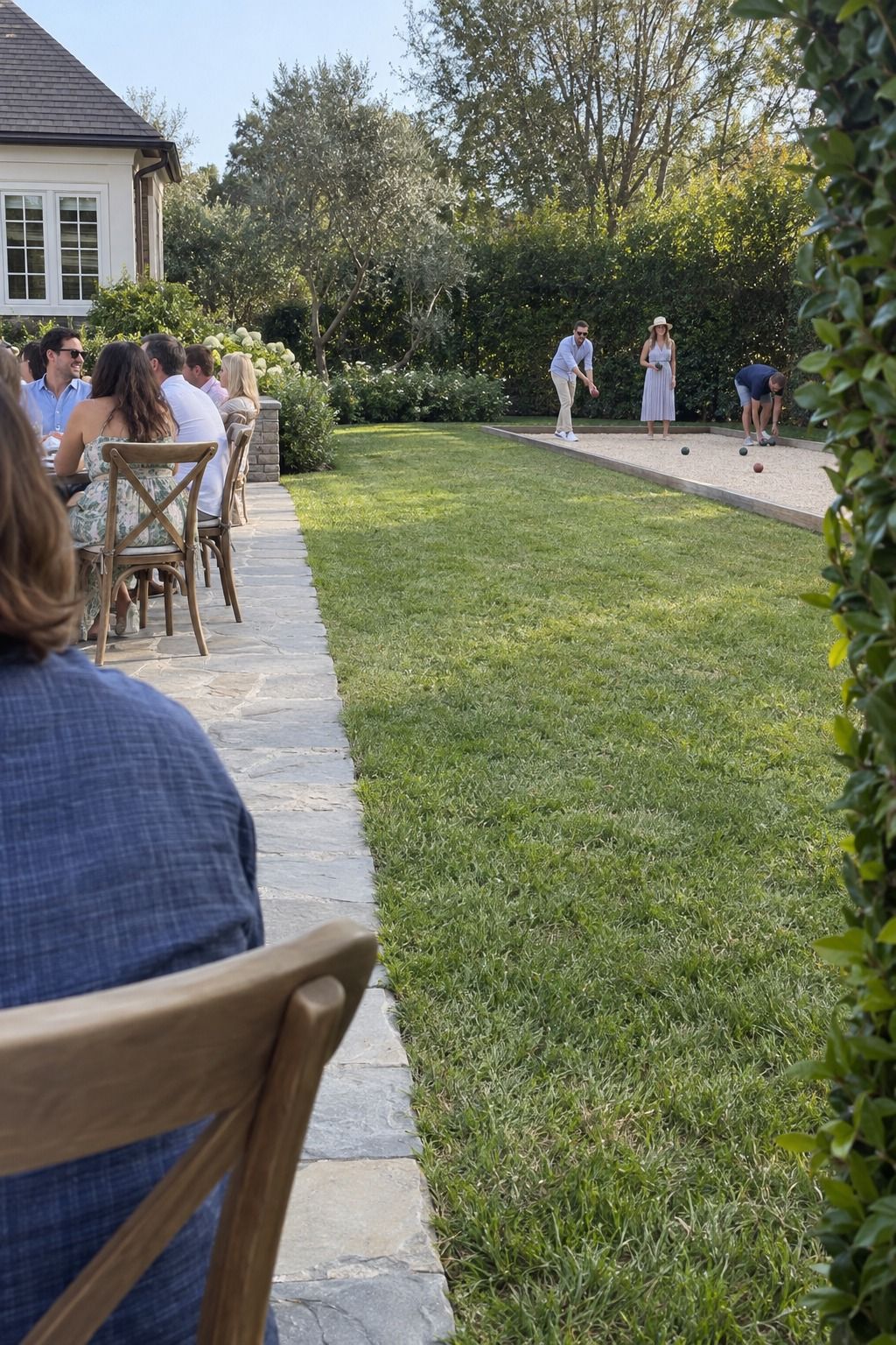 Guests begin one casual bocce game across a clear lawn buffer from the occupied dining patio.