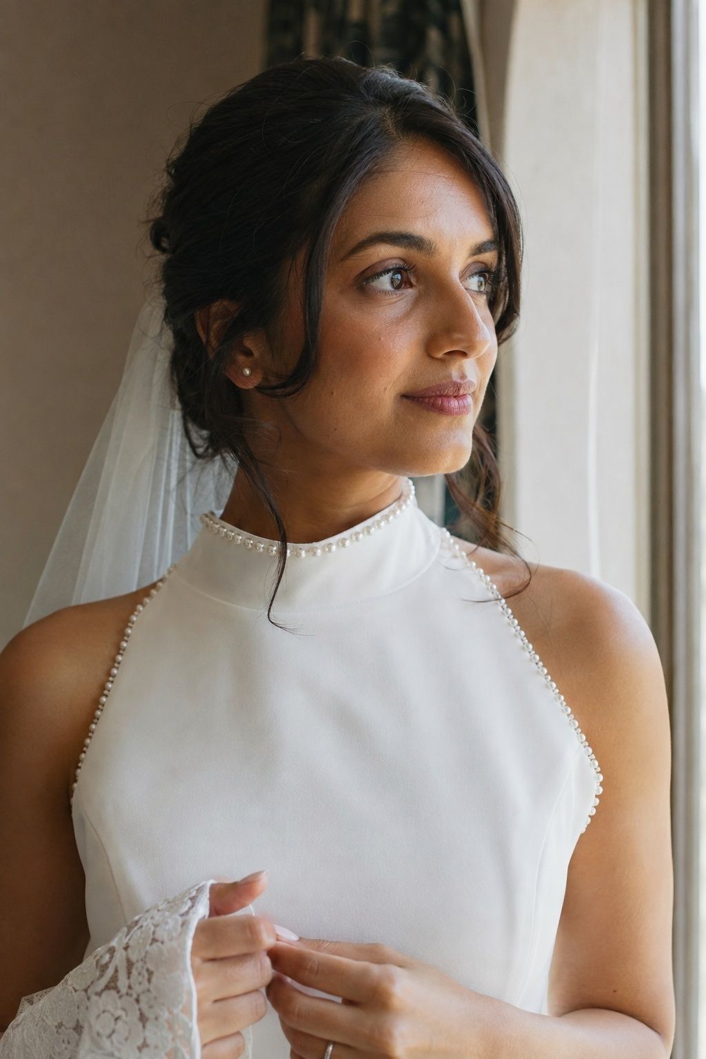 Chest-up adult South Asian bride in ivory high neck dress with tiny individual pearls sewn along collar and bodice edge