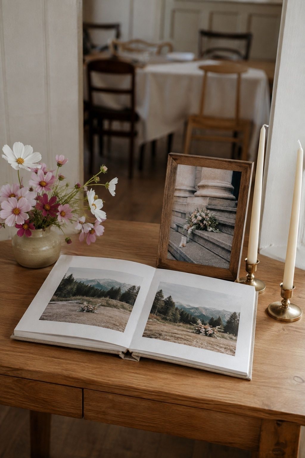 Open elopement album and framed bouquet photograph displayed with cosmos and brass candleholders.