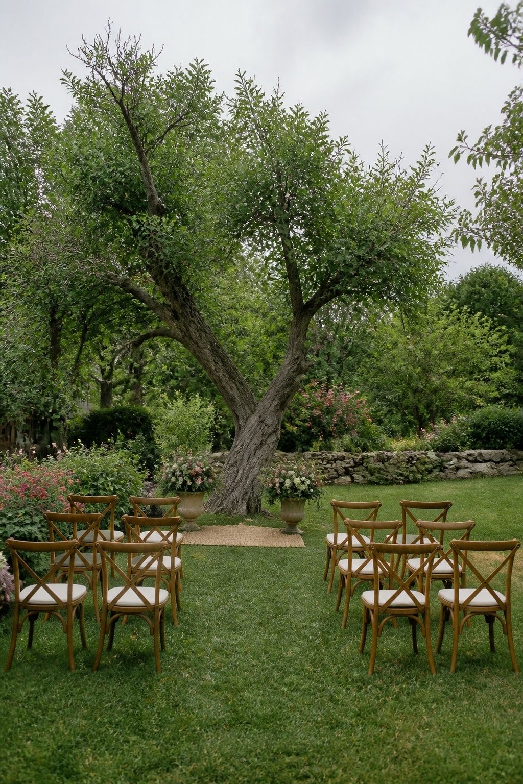 Small garden wedding ceremony with curved chair rows, a rug and two floral urns.