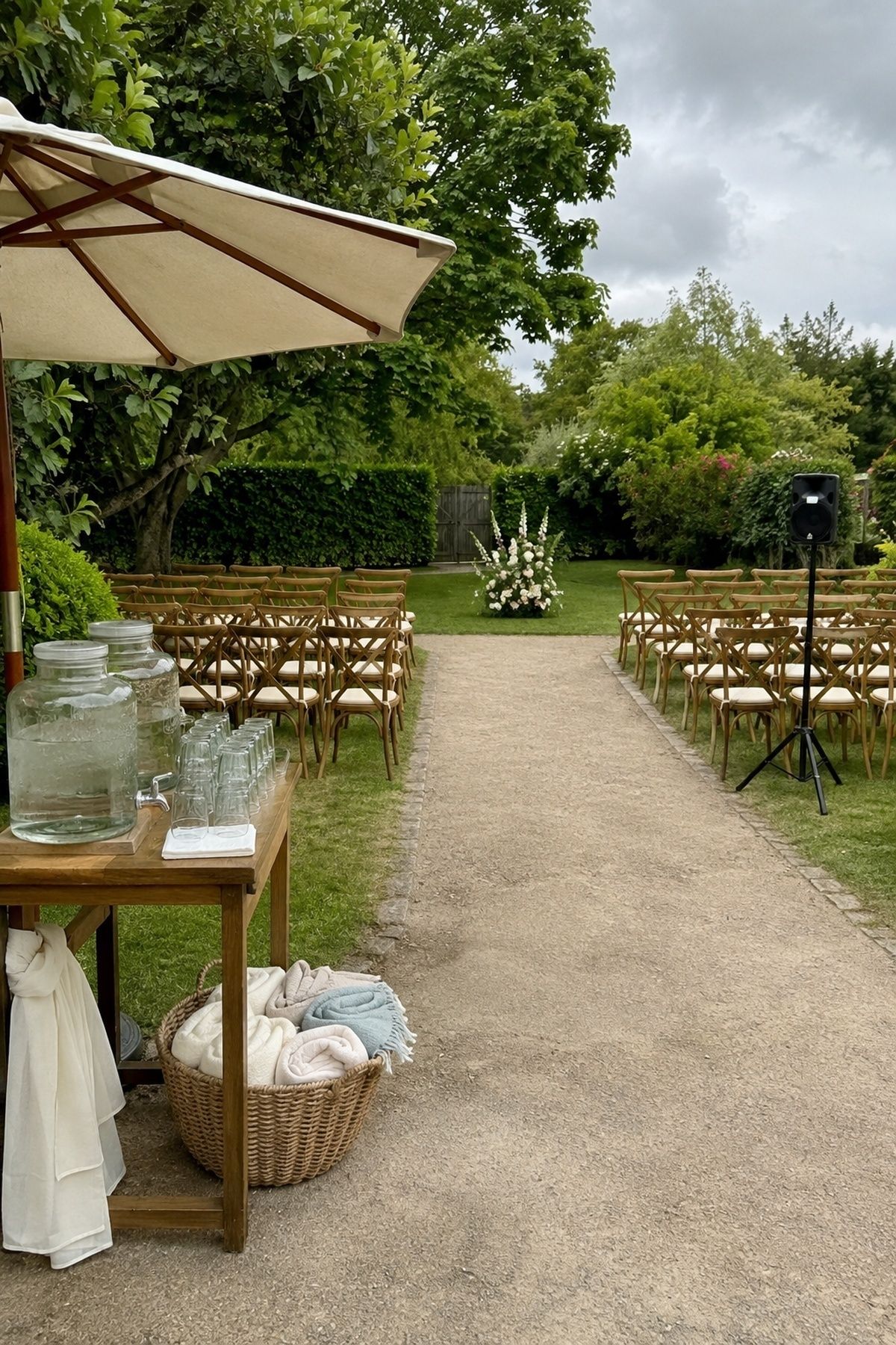 A modest garden ceremony setup with complete comfortable seating, a wide accessible aisle, shaded water station, discreet ceremony speaker, and basket of wraps, with only restrained floral decor. for a wedding under $20,000