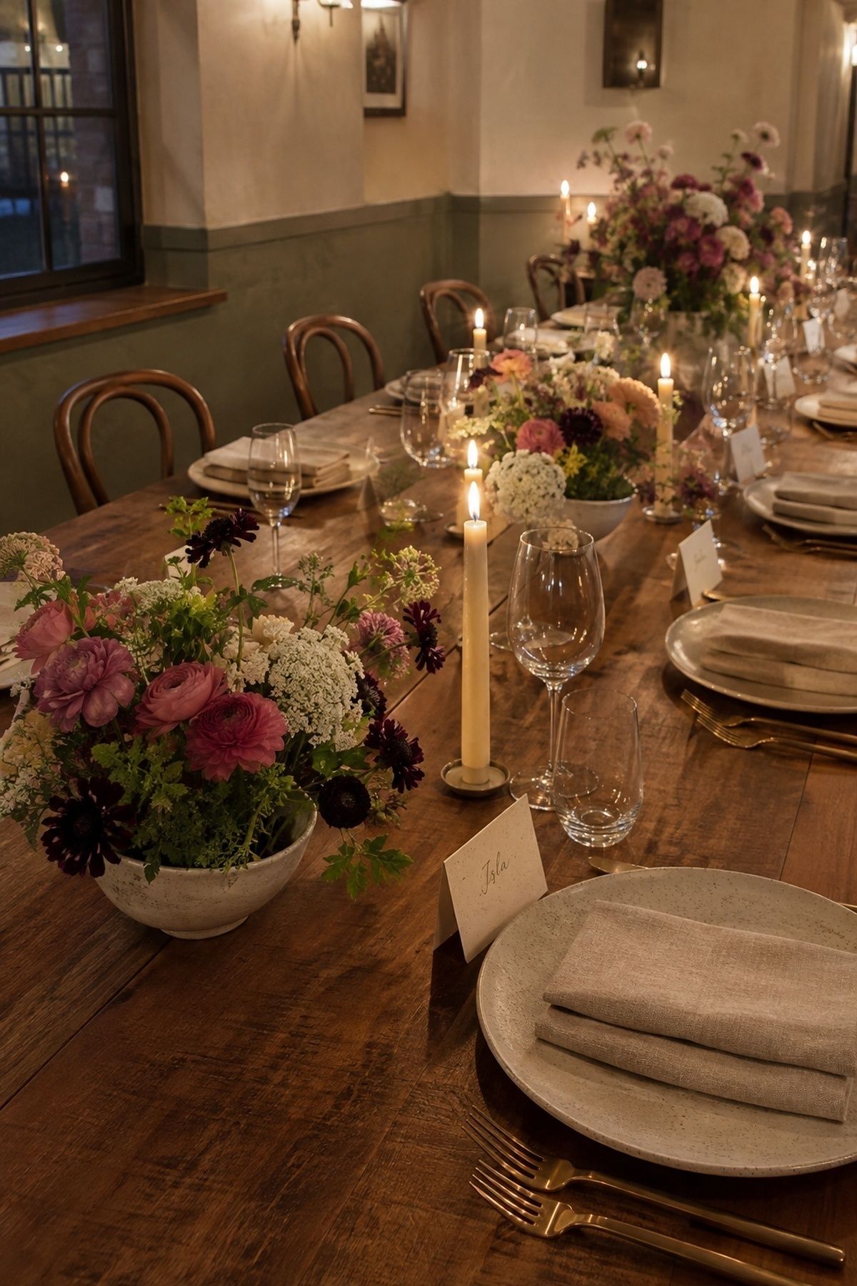 A low diagonal view along an intimate dinner table repeating low seasonal flower bowls, safe ivory tapers, oatmeal linen napkins, simple place cards, and one fuller floral focal point. for a wedding under $20,000