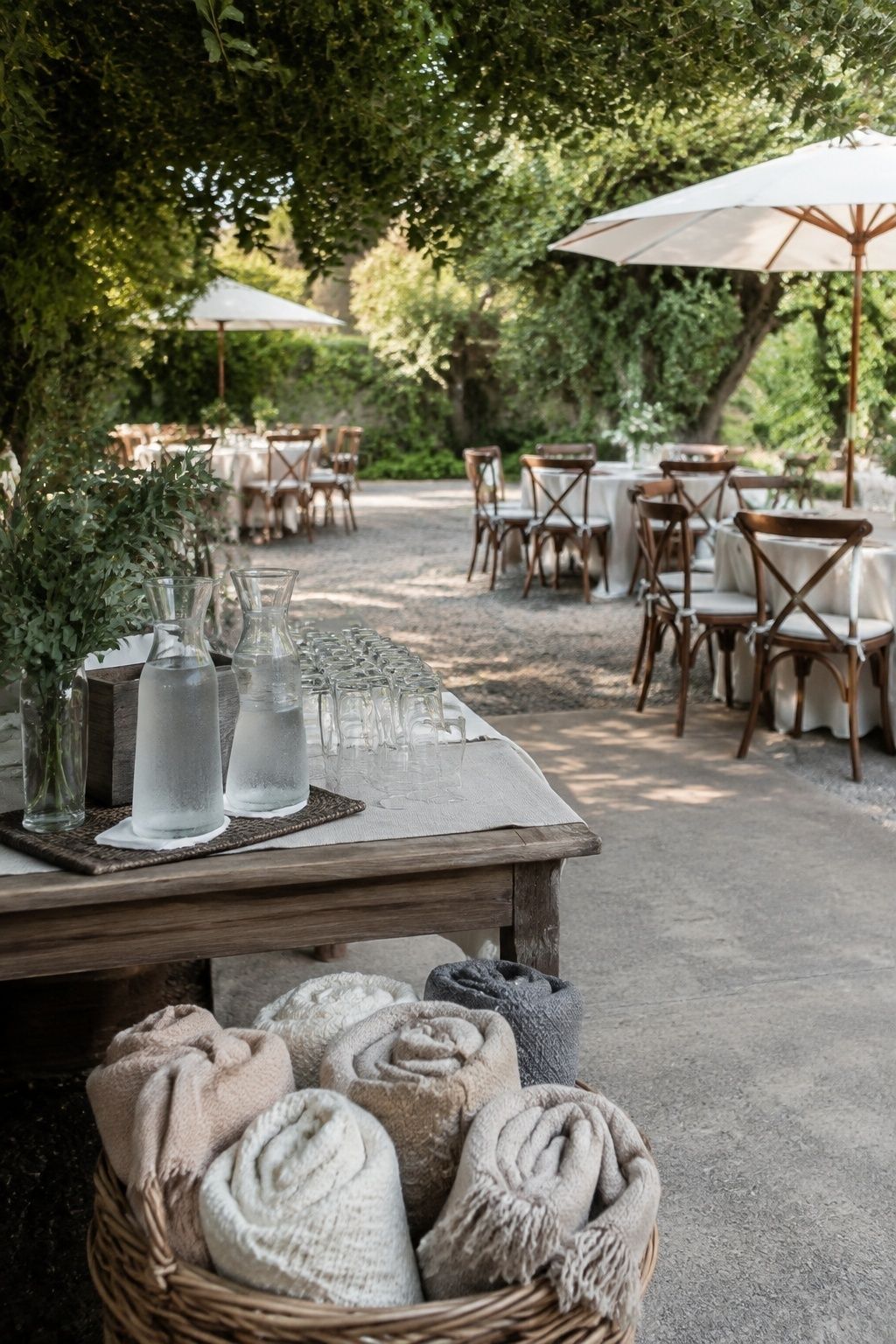 Shaded garden wedding reception with water carafes, comfortable chairs, clear walkway, parasols, and folded shawls