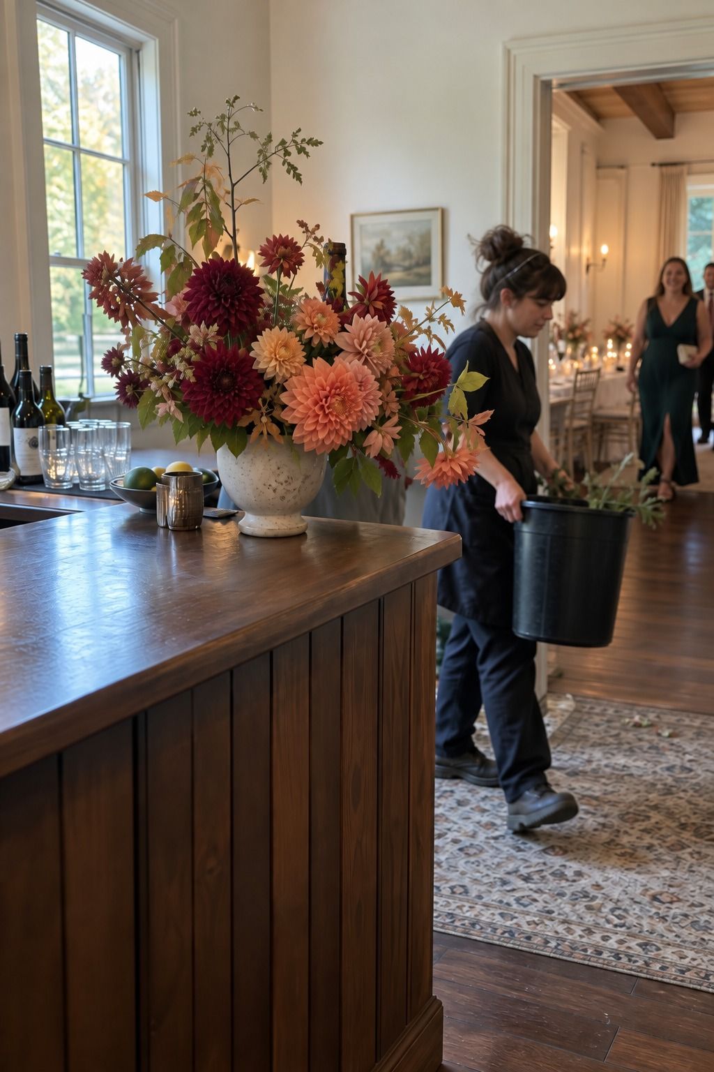 A coordinator carries away an empty bucket after placing one concentrated dahlia arrangement on a quiet bar end.