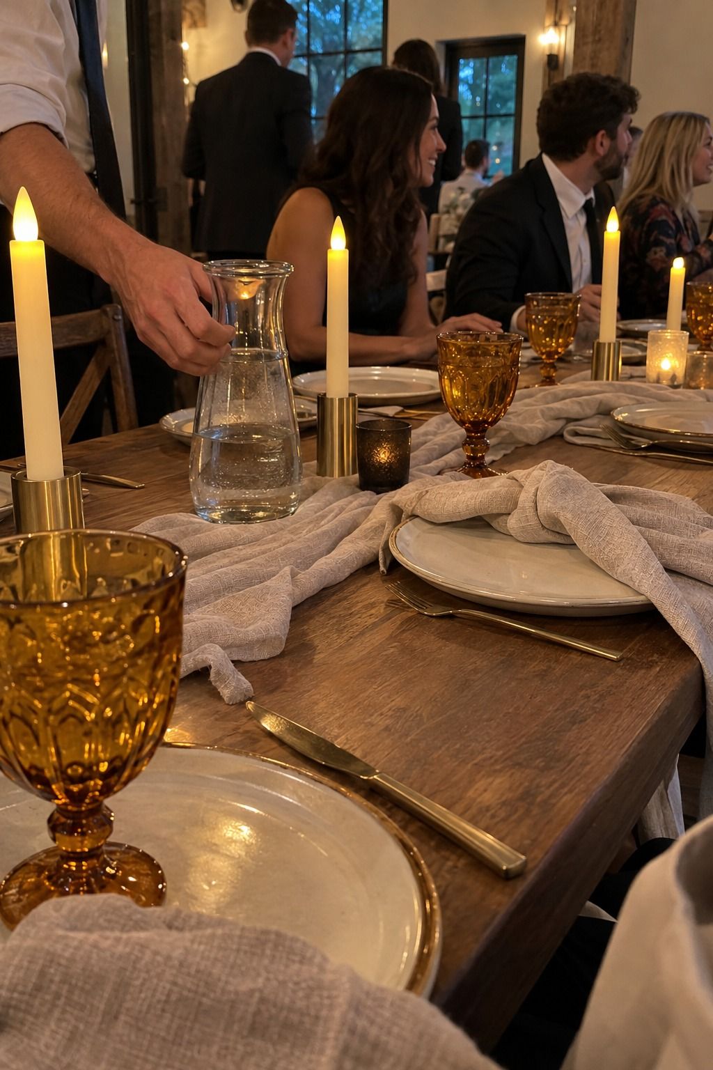 Amber goblets catch warm light at an occupied table using clearly flameless rechargeable tapers and no botanicals.