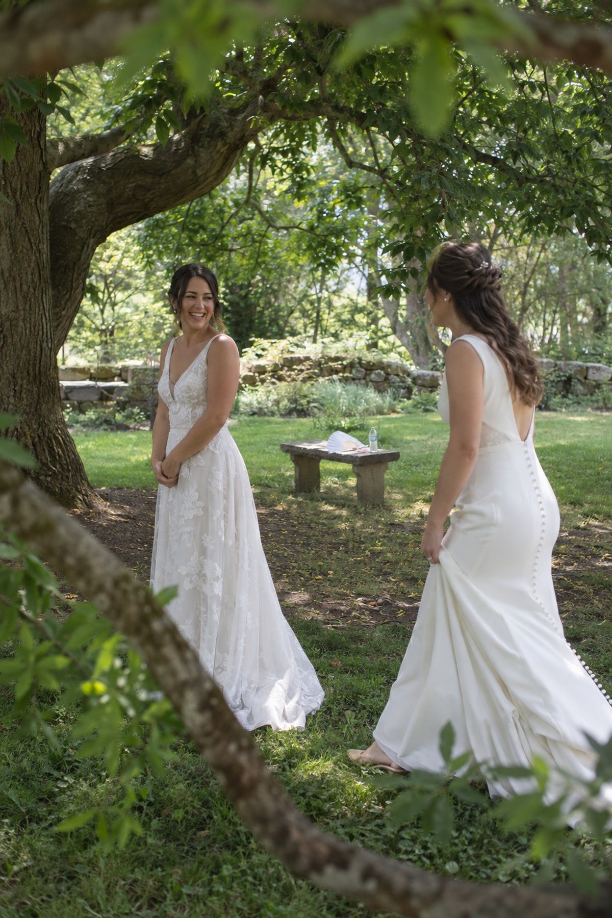 Two brides share a private first look beneath mature trees at a July wedding.