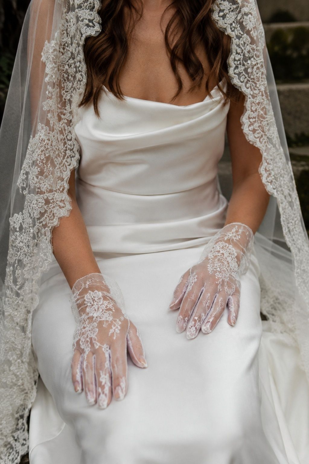 Sheer lace gloves resting on a satin gown beneath a mantilla