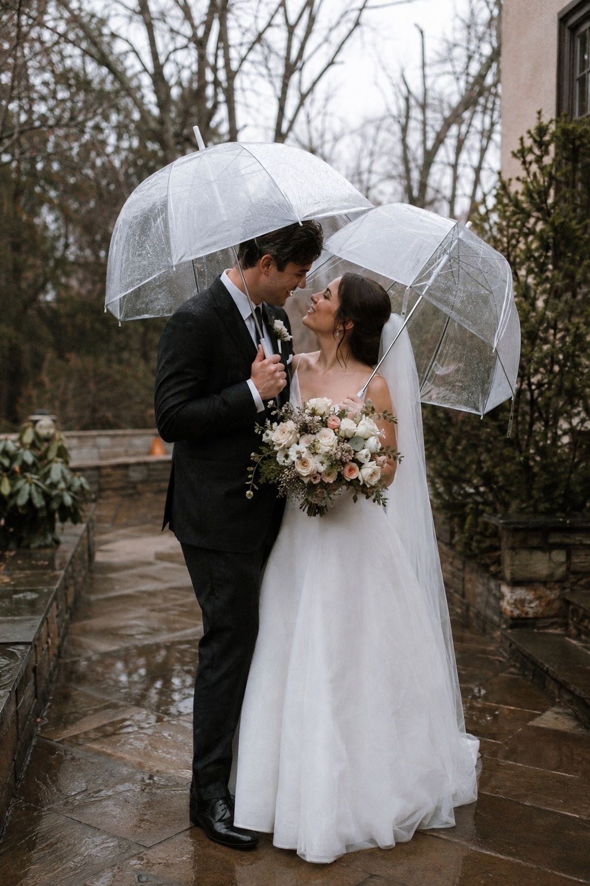 March wedding couple under clear umbrellas during light rain on a wet stone path