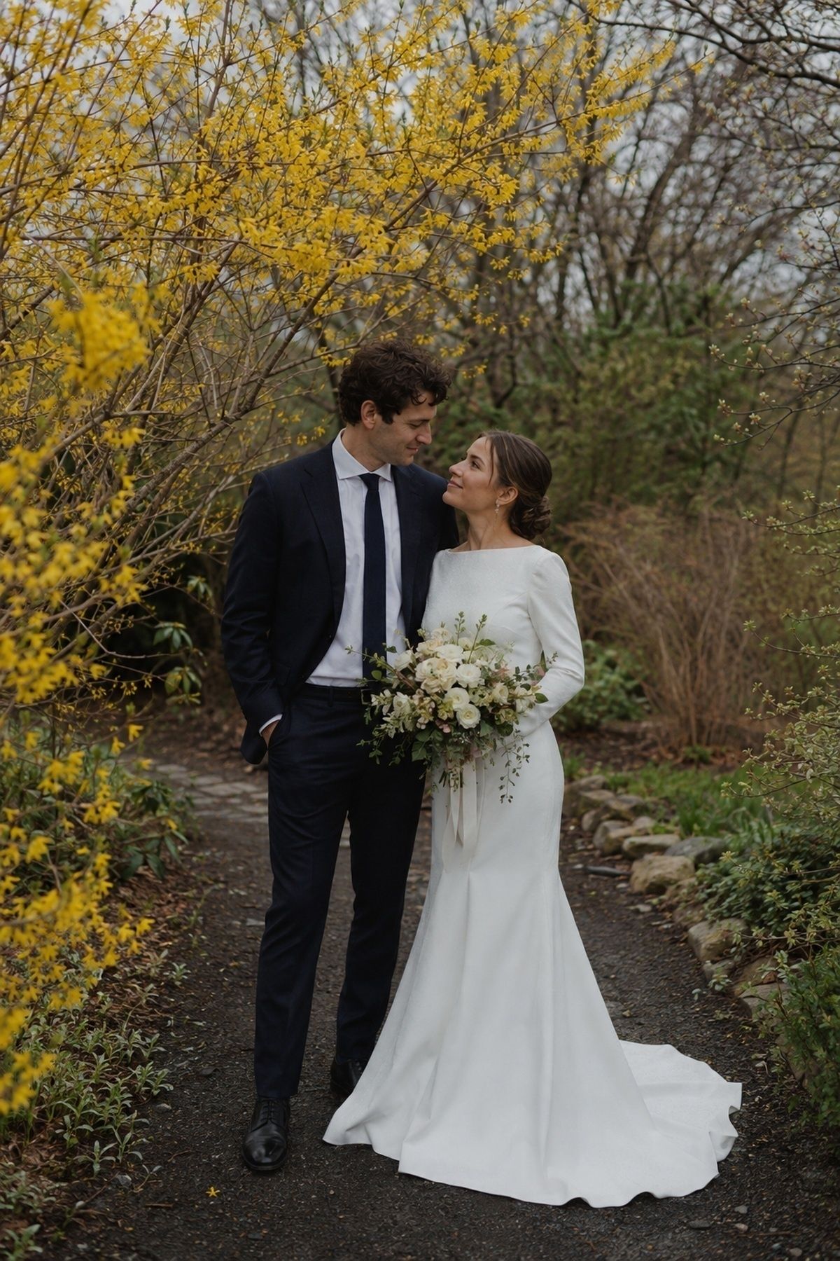 March wedding portrait with forsythia and budding branches on a damp garden path