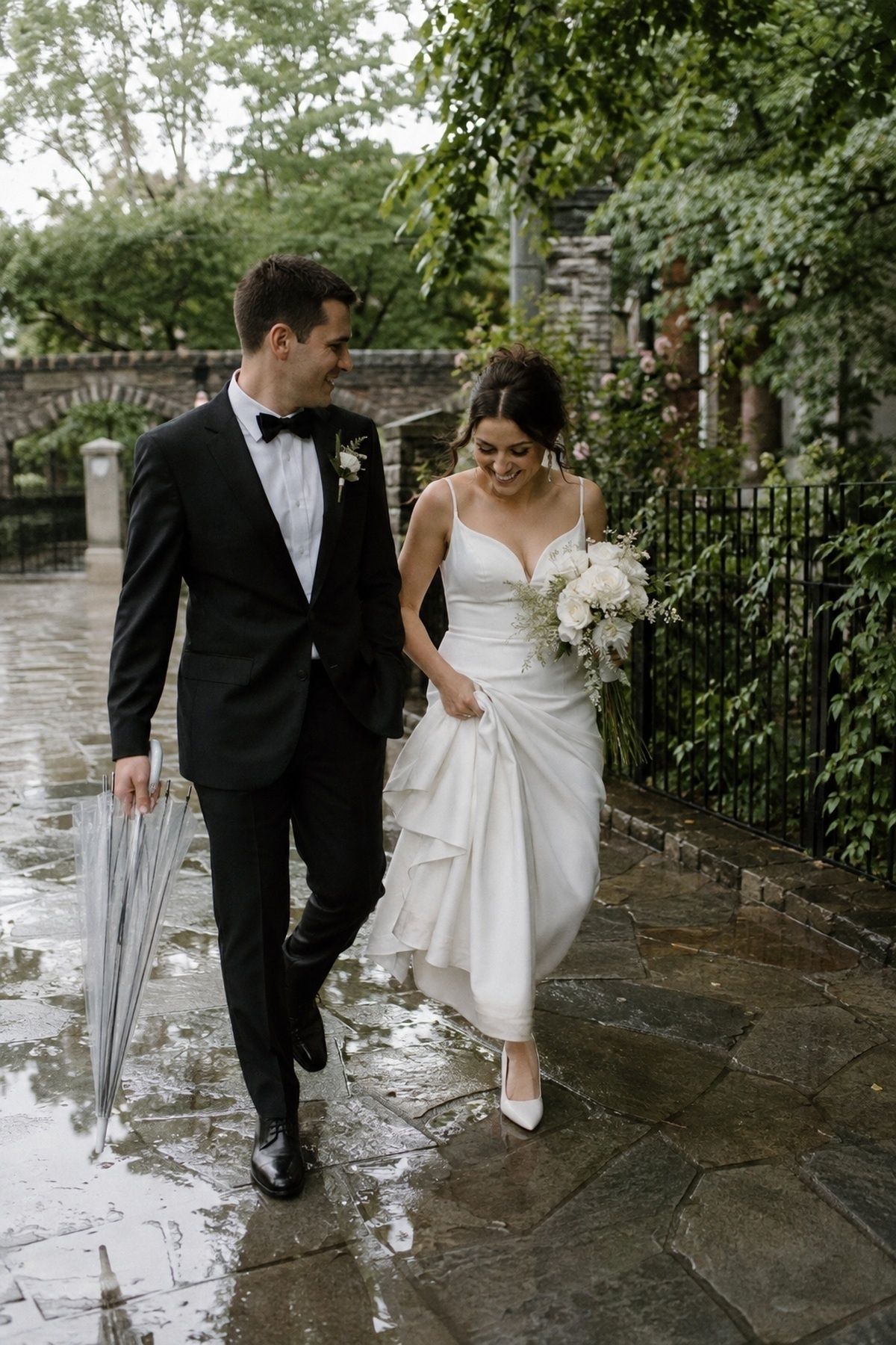 March wedding couple walking on a wet stone path after rain with a folded clear umbrella
