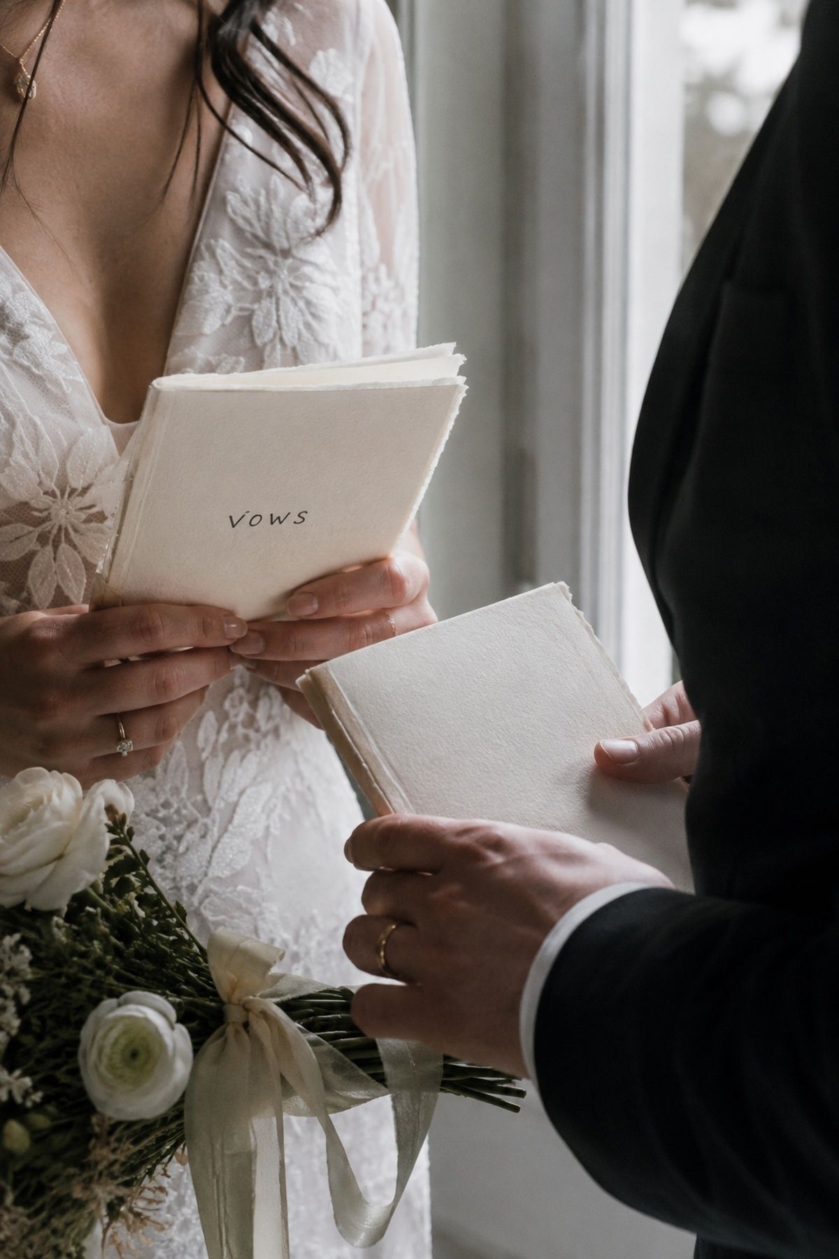 March wedding vow booklets held by the couple with rings, bouquet, and soft window light