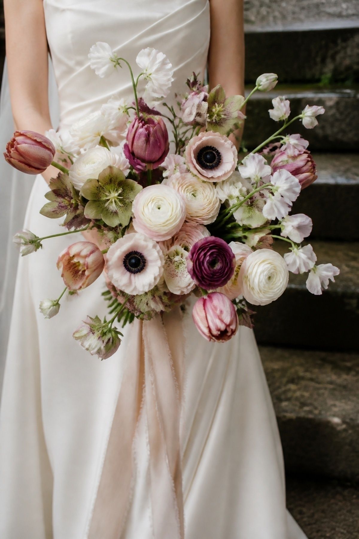 March wedding bouquet with ranunculus, anemones, hellebores, tulips, sweet peas, and trailing ribbon
