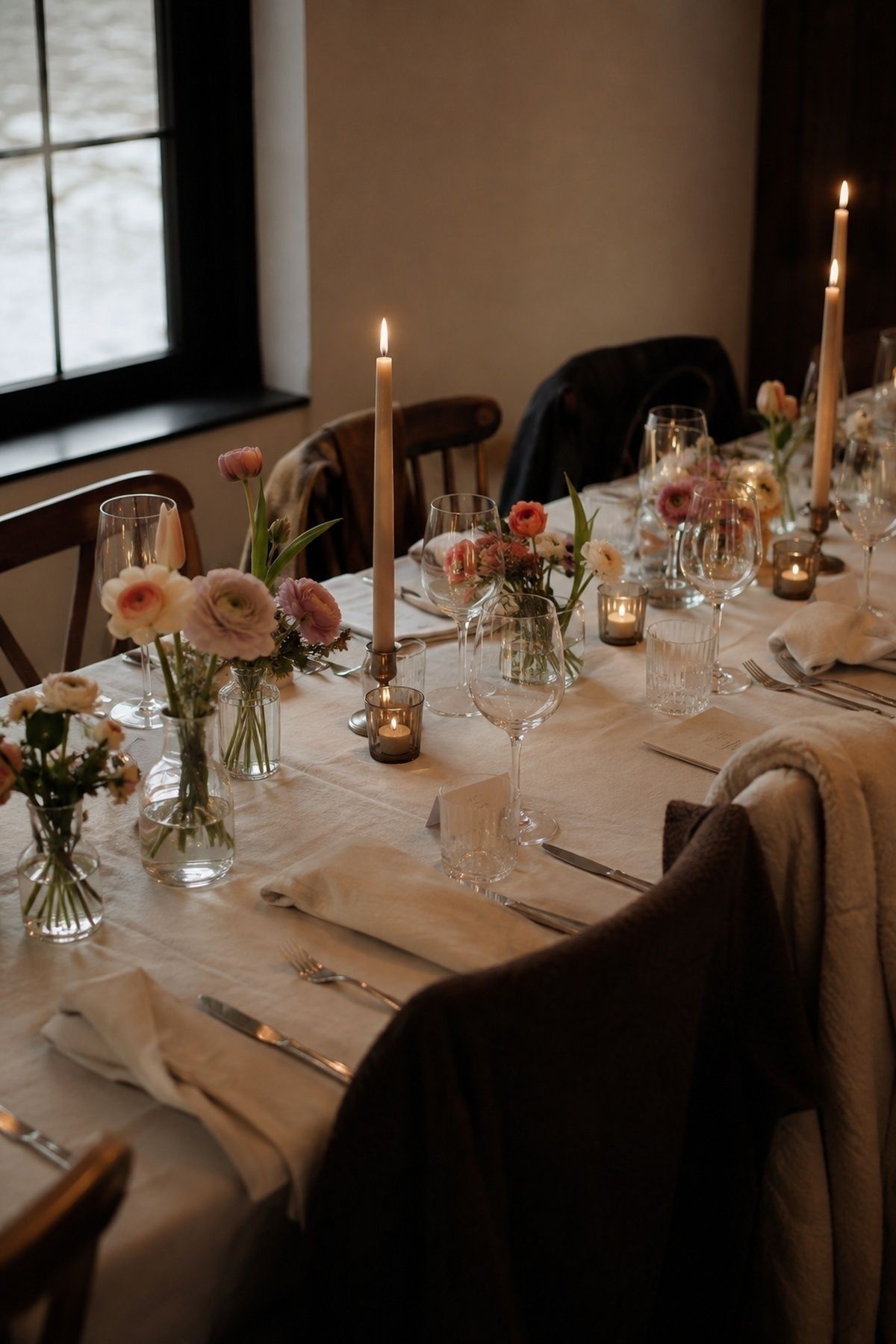 Intimate March wedding dinner table with candles, spring flowers, glassware, menus, and coats nearby