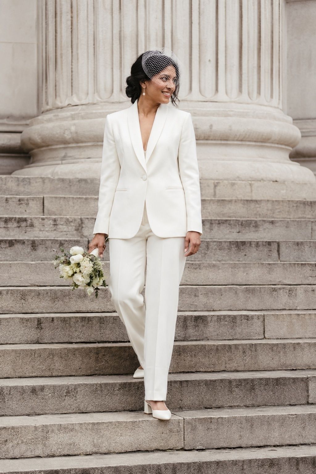 Bride in an ivory trouser suit and low heels on pale stone steps