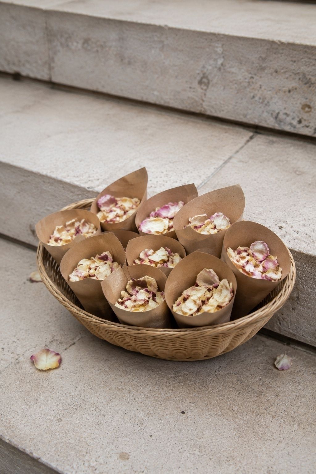 Kraft cones of dried petal confetti in a small basket on stone steps