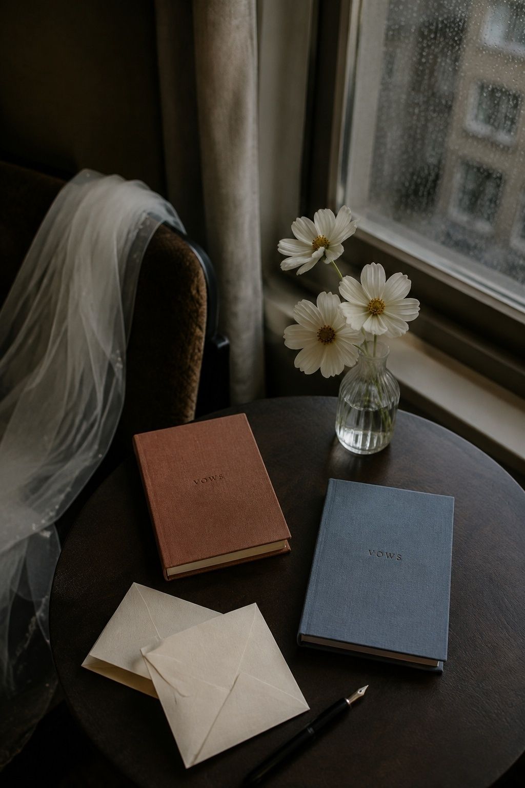Terracotta and blue vow books with letters beside a rainy hotel window