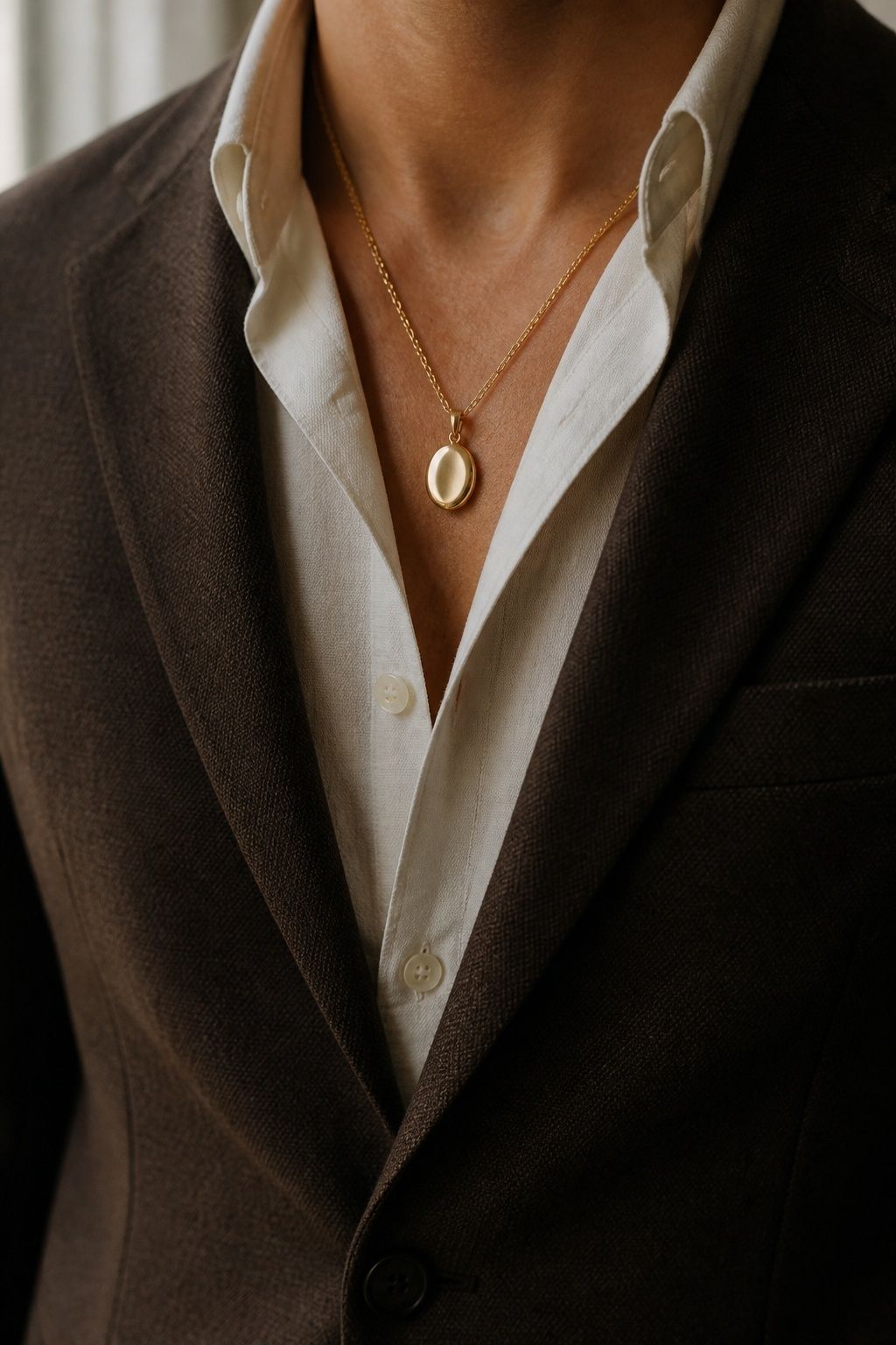 Small flat oval heirloom pendant worn at an ivory shirt neckline under a brown wedding jacket