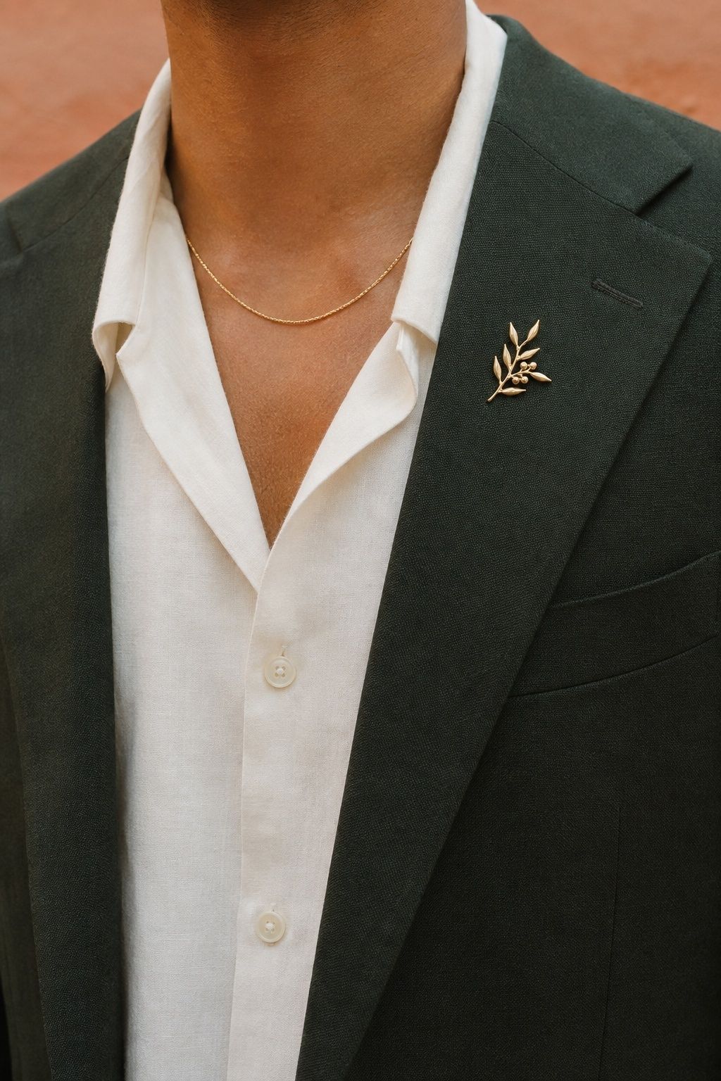 A delicate gold necklace separated from a small botanical gold brooch on a green wedding jacket lapel