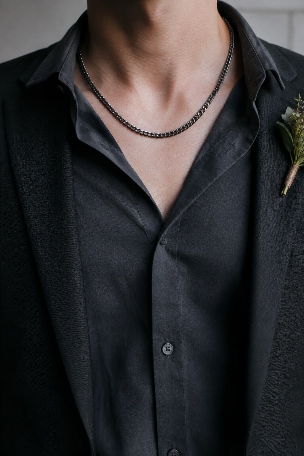 Brushed matte gunmetal chain against a dark modern wedding suit, softly lit to show low-shine texture