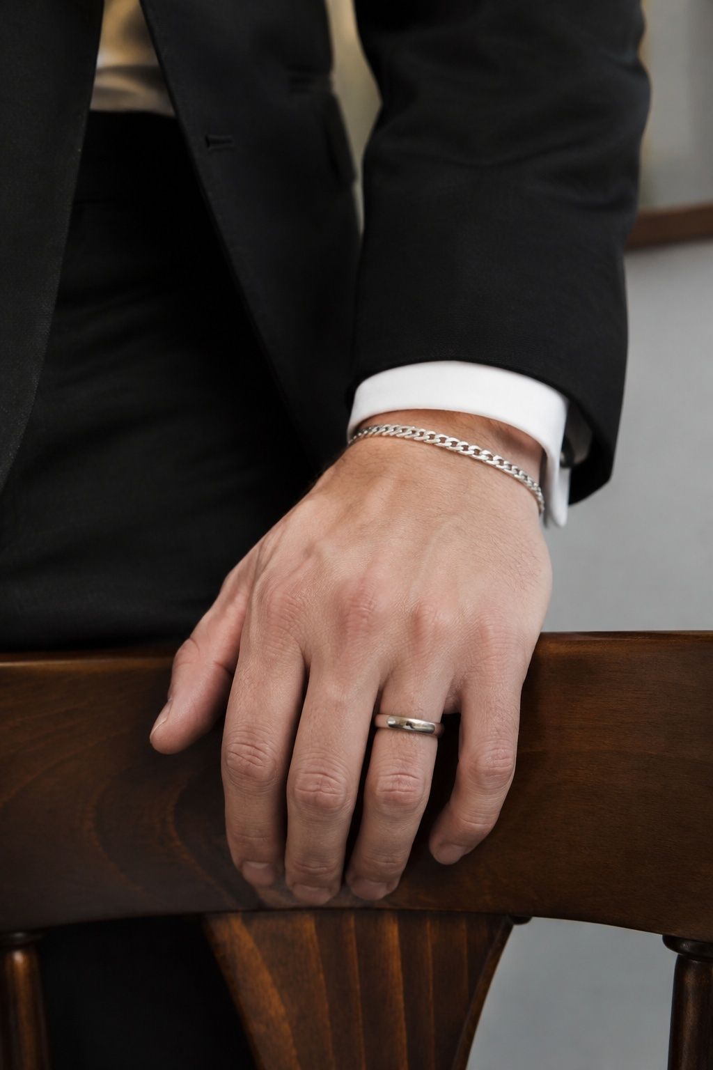 Groom's narrow silver chain bracelet worn with a black suit
