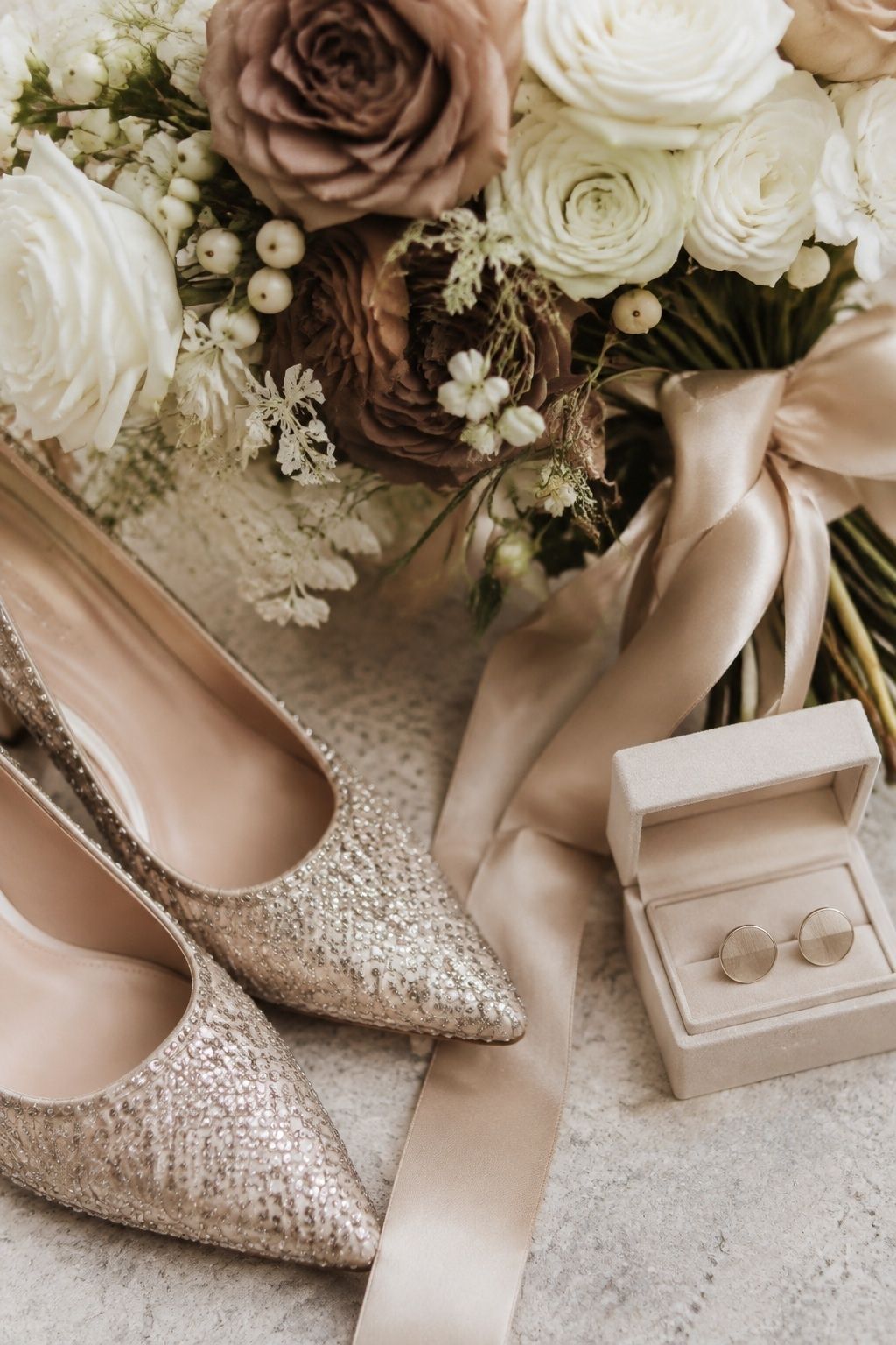 Champagne beaded bridal shoes and cufflinks beside cream flowers and satin ribbon.