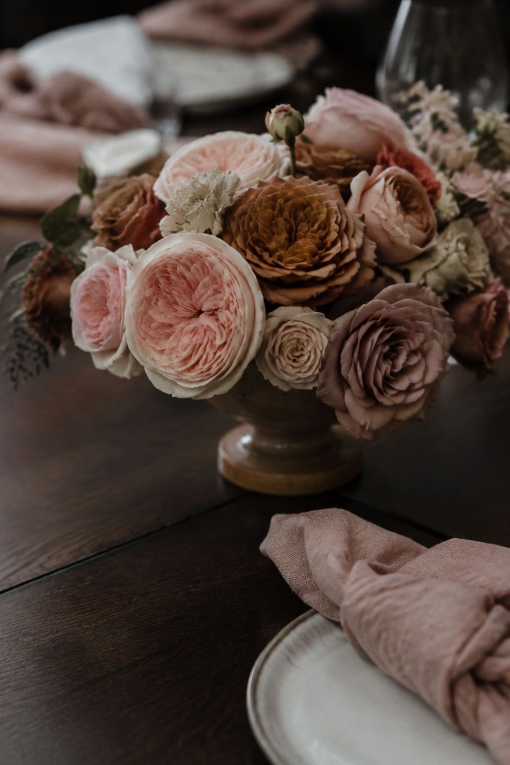 Blush and mocha garden roses in a low centerpiece beside dusty pink linen.