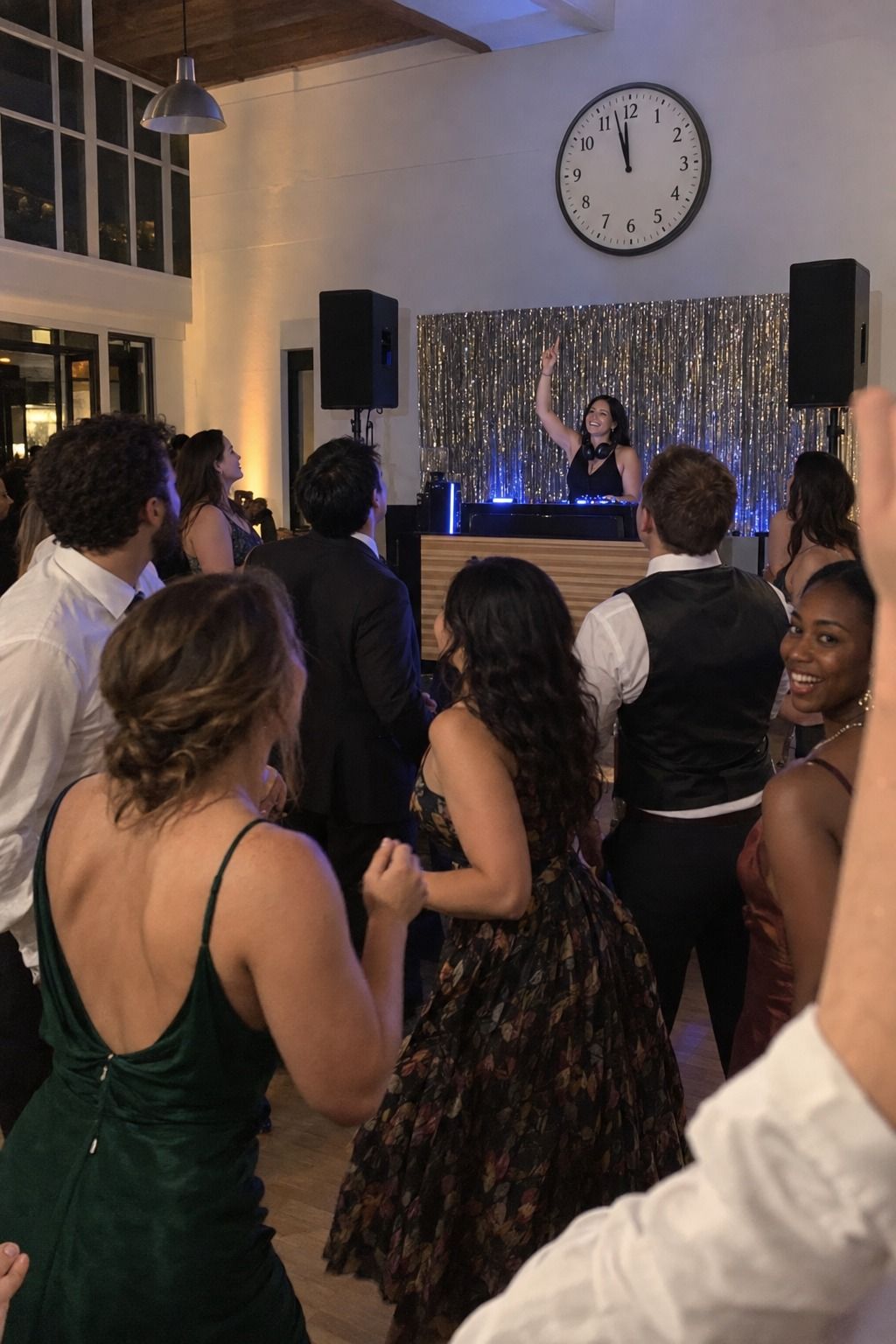 Guests naturally turn toward a DJ beneath one large analog clock showing nearly midnight, with every face unobstructed.
