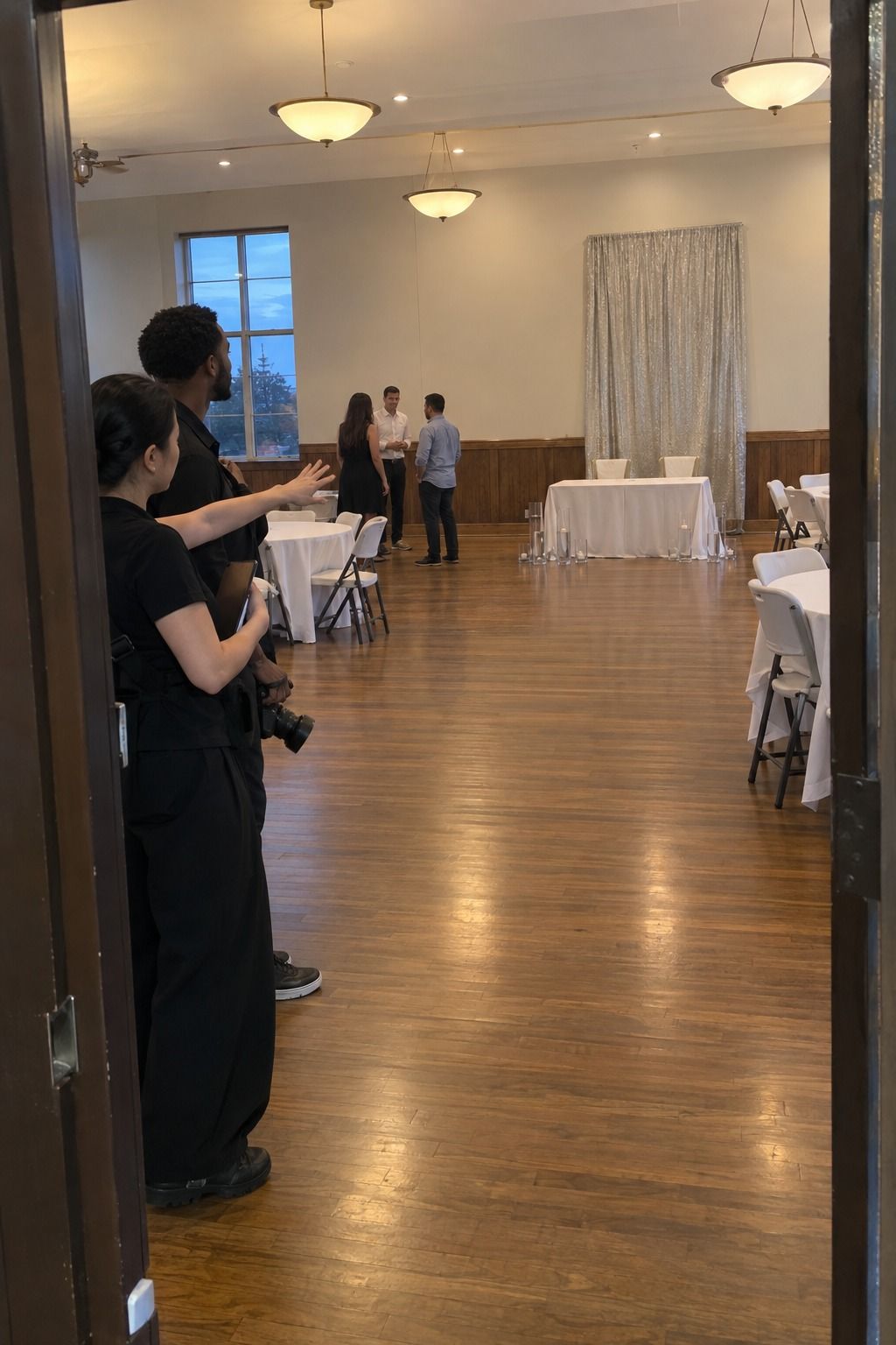 A coordinator and photographer test an unobstructed layered view from the doorway toward an empty sweetheart table and silver wall detail.