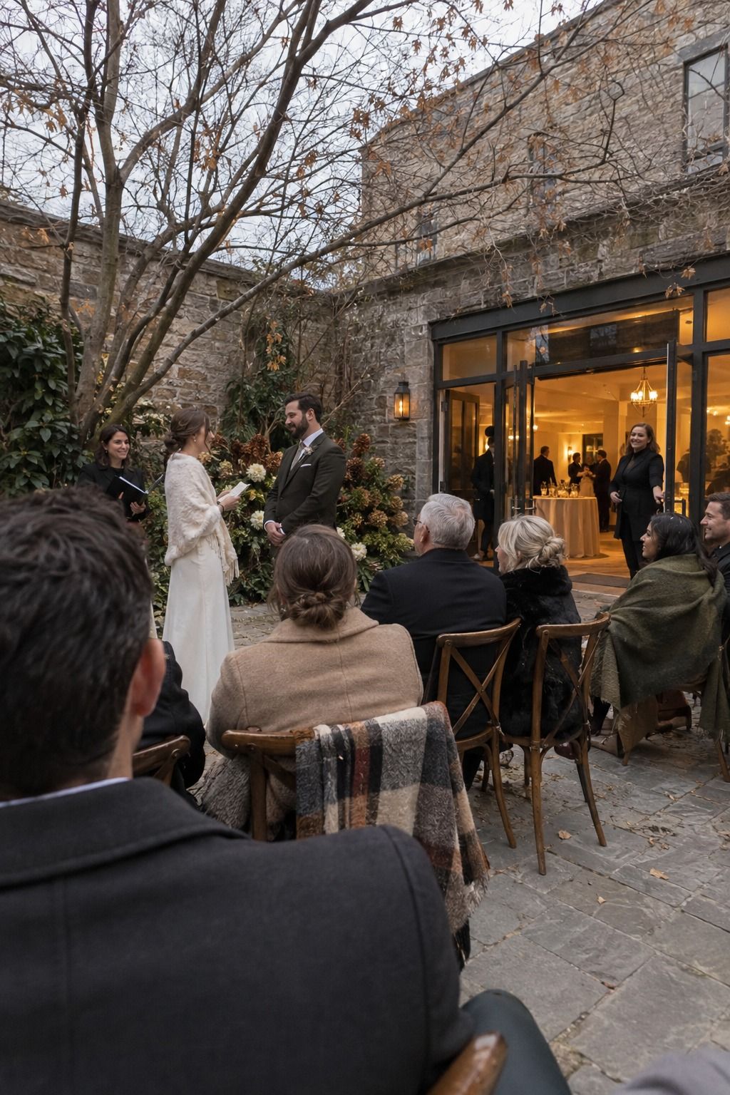 Coated guests attend a short November courtyard ceremony beside the warm indoor reception doorway.