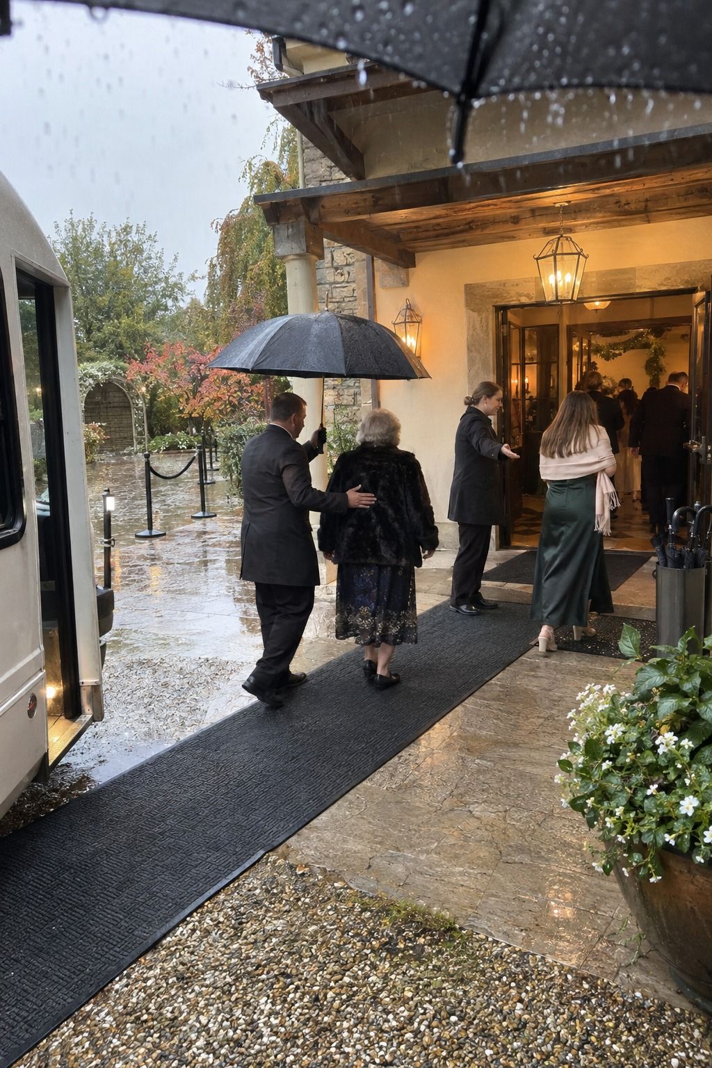 Wedding staff guide guests along a dry covered backup route from a shuttle to the venue during cold November rain.
