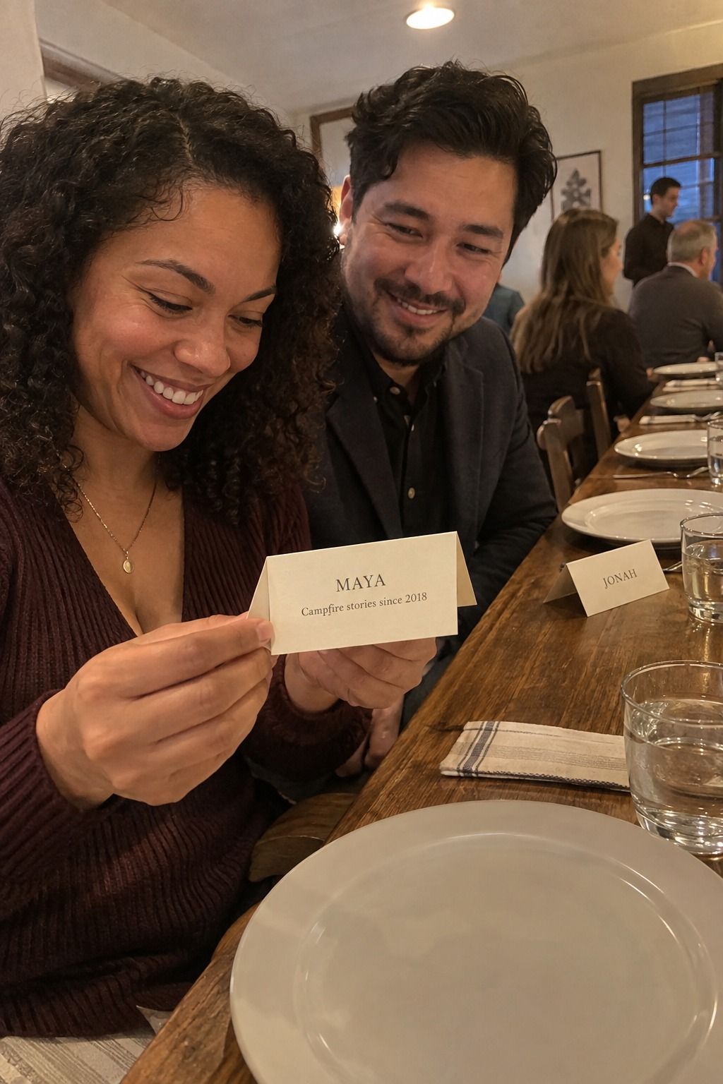 Two guests smile over a legible card reading MAYA and Campfire stories since 2018, with JONAH visible at the next setting.