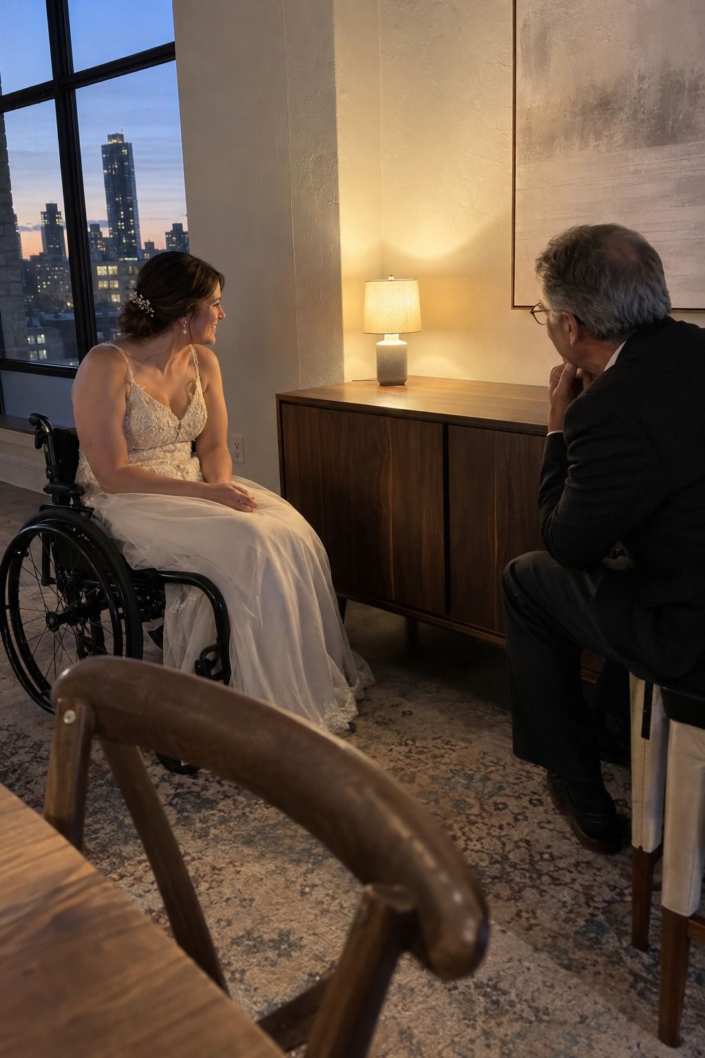 A wheelchair-using bride and older coordinator test a small cordless shaded lamp from seated height on a broad sideboard away from service and heat.