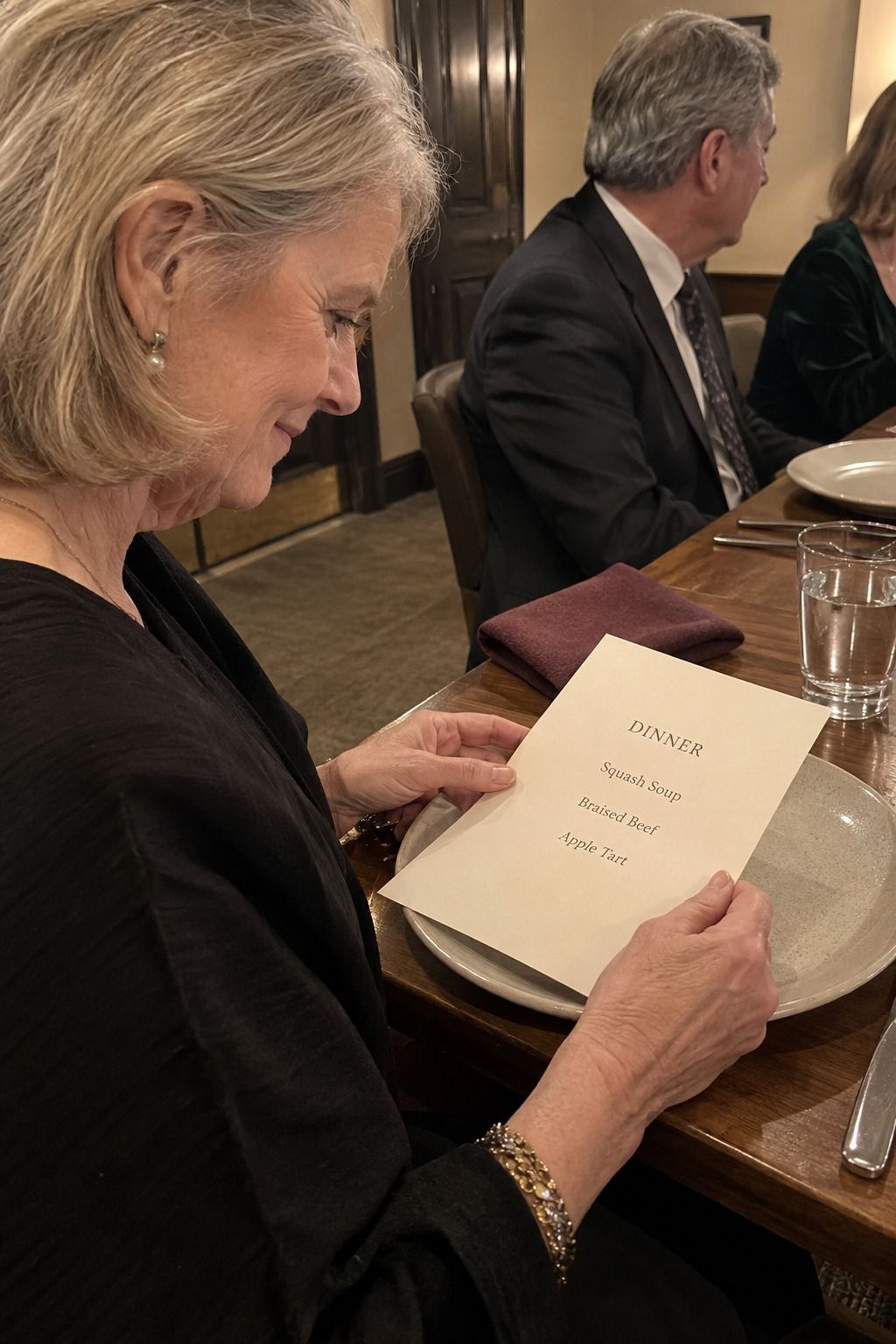 An older guest reads a plate-set menu with the exact legible courses DINNER, Squash Soup, Braised Beef, and Apple Tart.