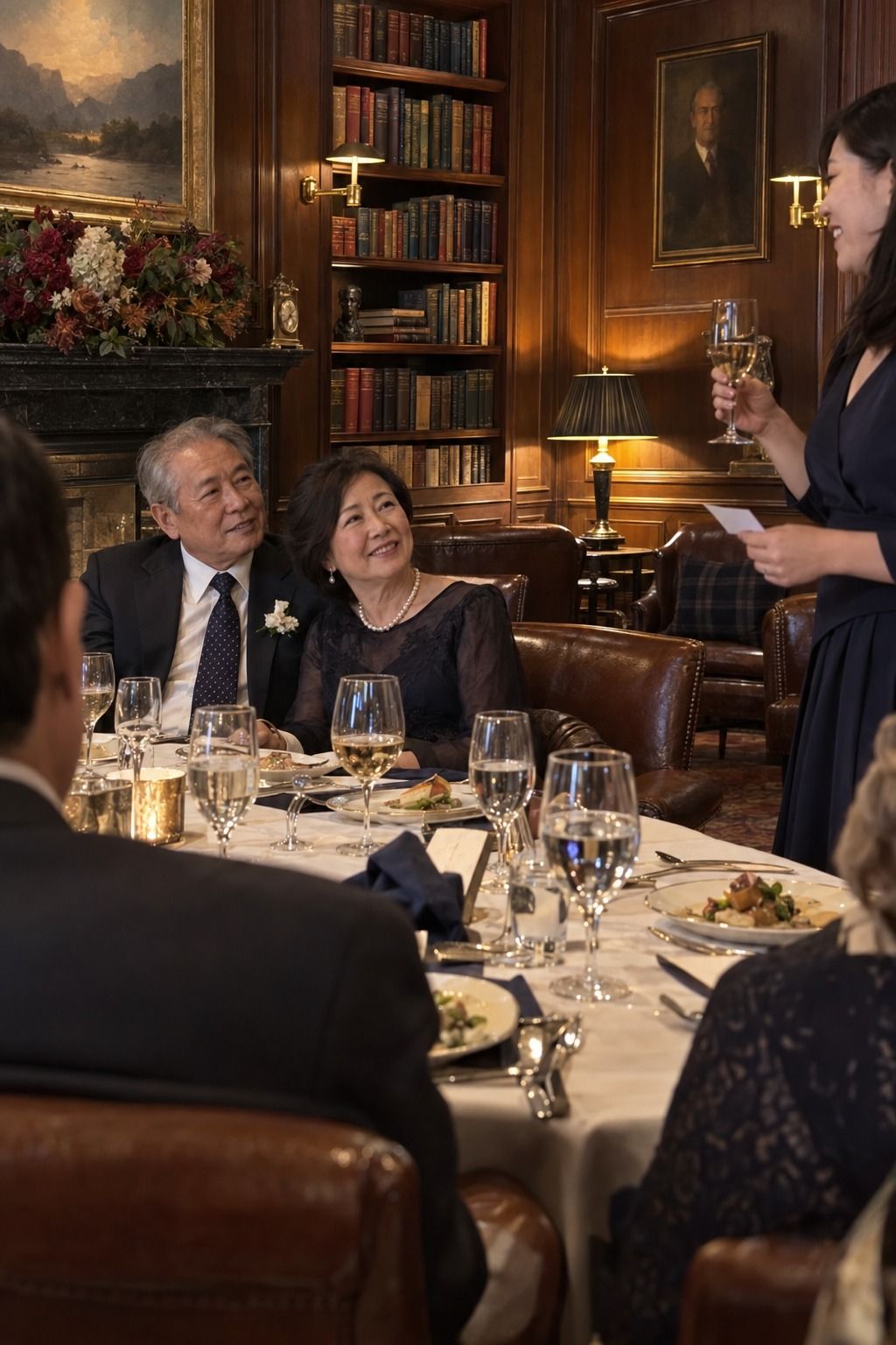 An older East Asian newlywed couple listens to their daughter's toast in a book-lined private club library.