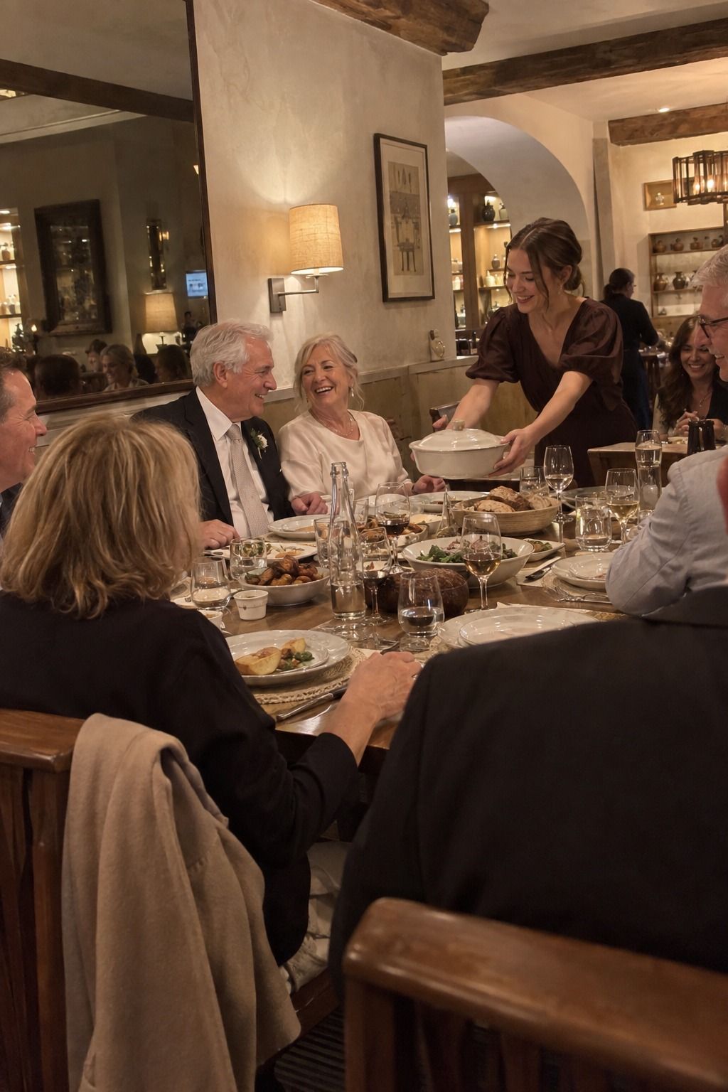An older newlywed couple laughs as a niece brings a covered dish to a flower-free restaurant table.