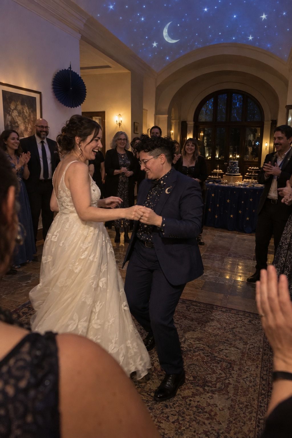 A bride and nonbinary spouse begin dancing beneath a subtle moon-and-stars ceiling projection.