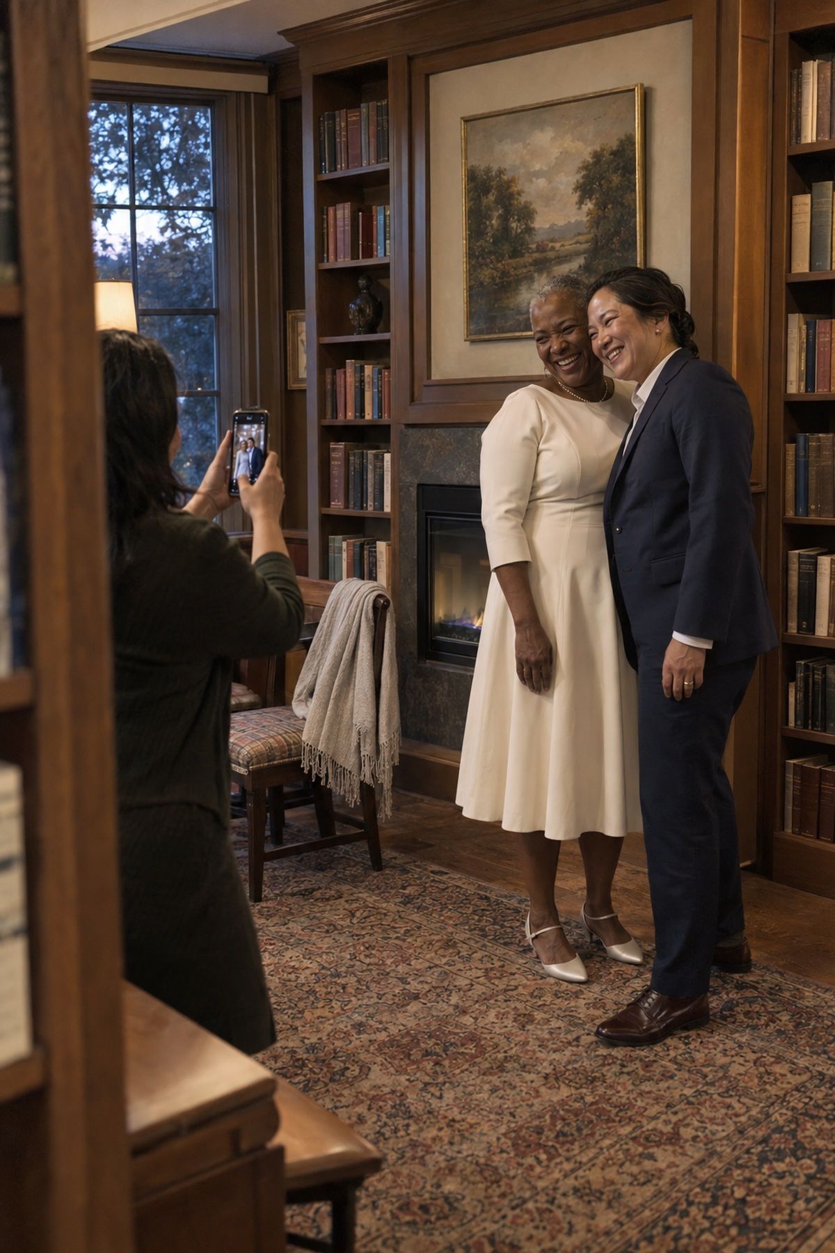 Two newlywed women pose for a quick private-room portrait beside a closed fireplace.