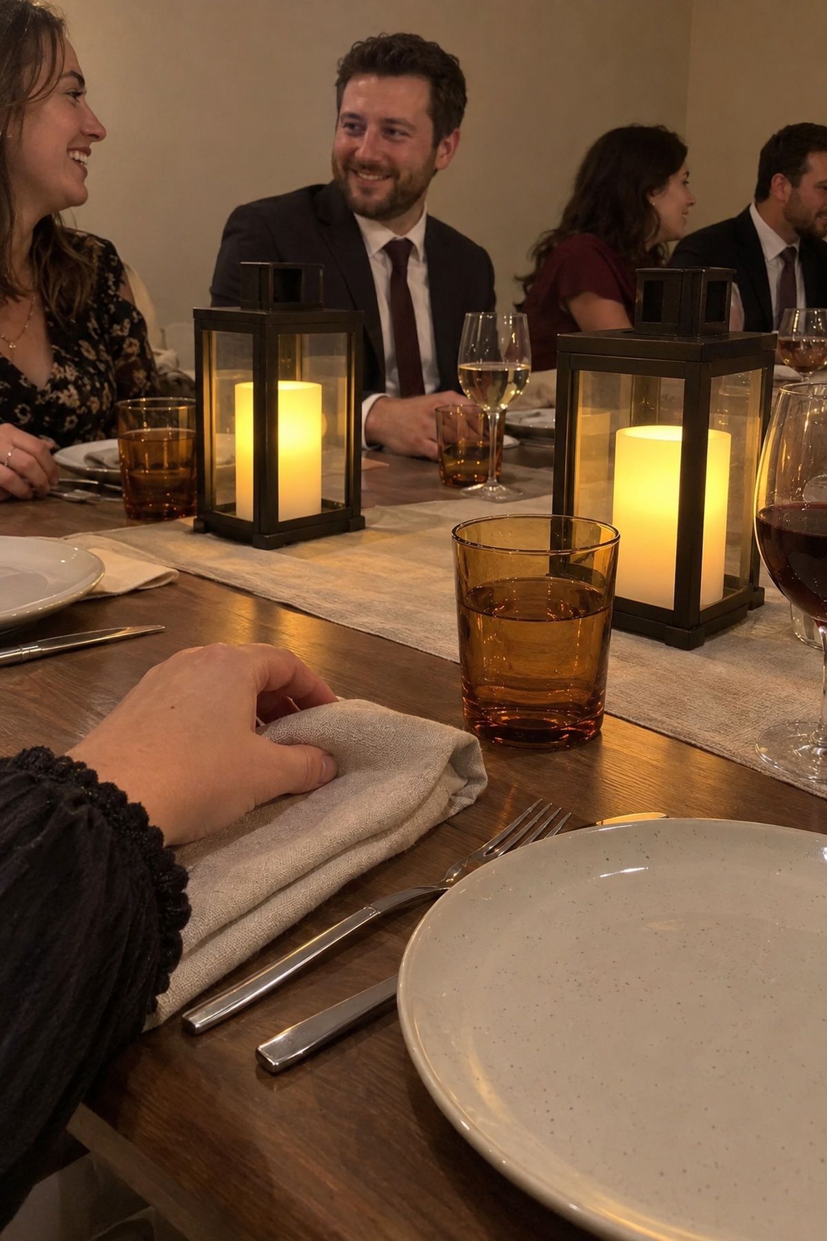 A guest adjusts a place setting beside enclosed battery lanterns at an October wedding dinner.
