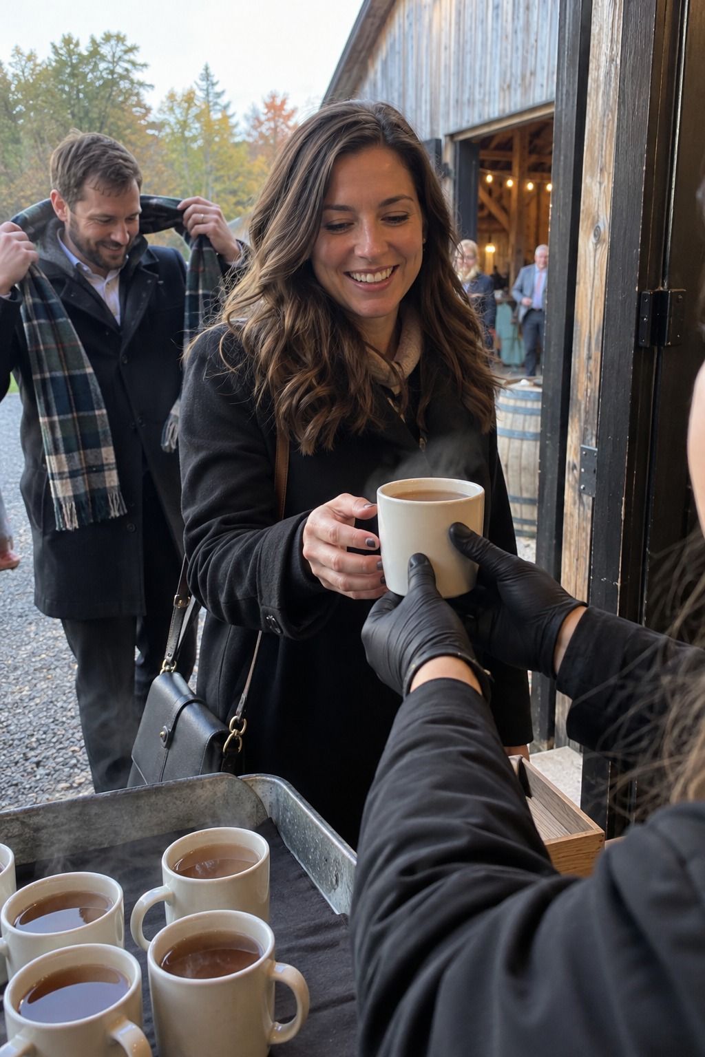 A warm cider handoff welcomes a wedding guest arriving from the October chill.