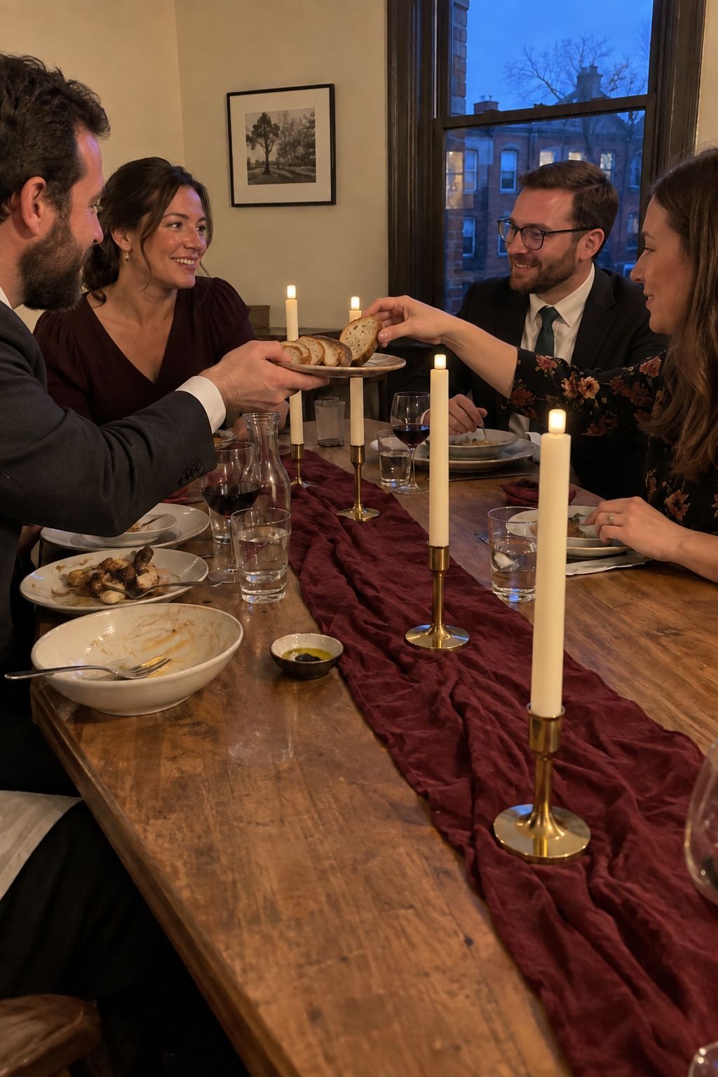 Occupied restaurant dinner with a narrow burgundy runner and unmistakable blunt-cap ivory electric LED tapers while four guests pass bread.