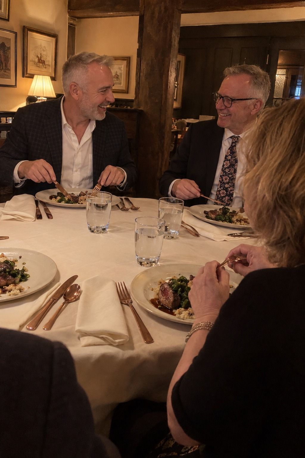 Older gay couple and a friend dine with copper flatware, ivory plates and soft cream cloth napkins in a country-pub room.