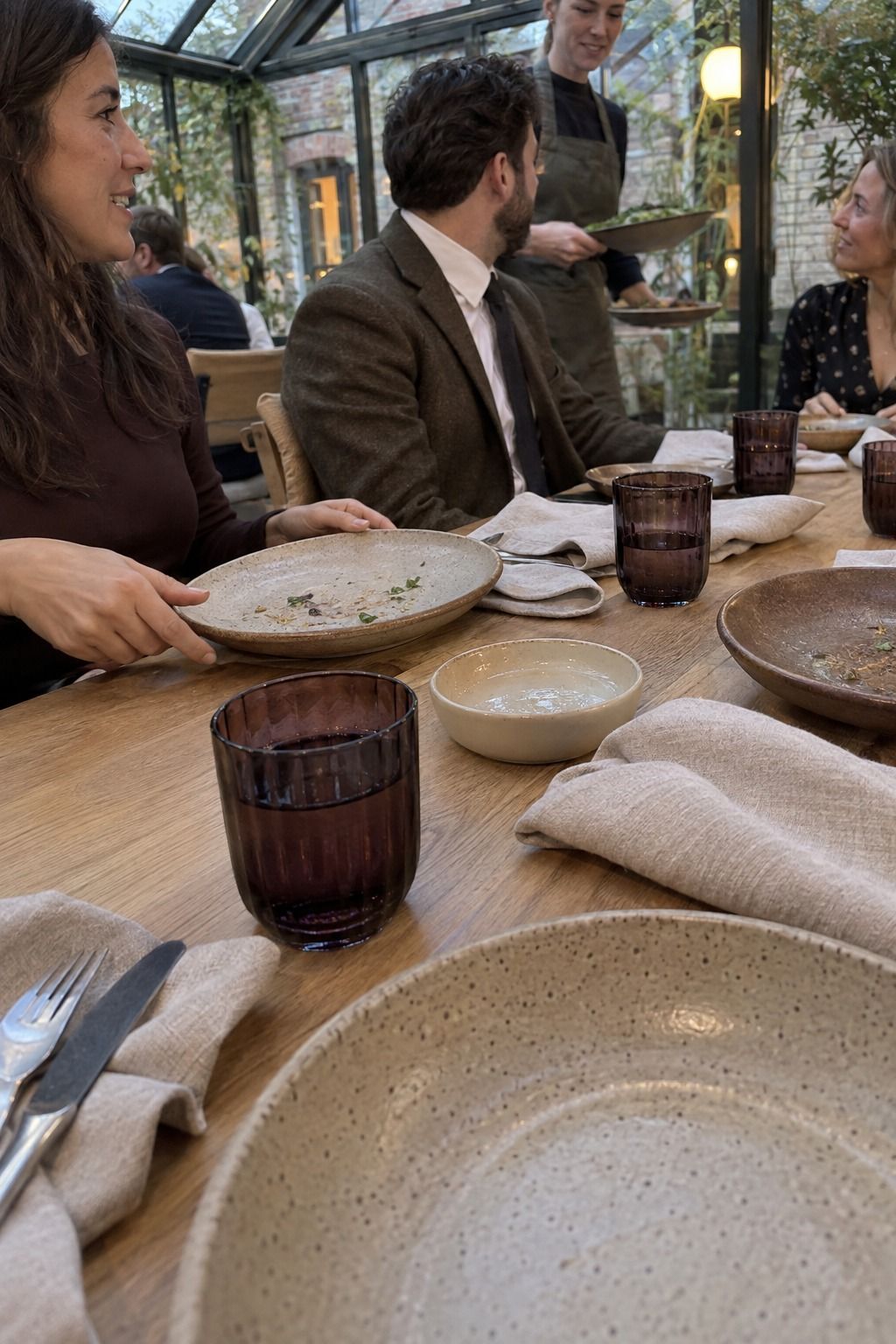 Conservatory dinner with used hand-thrown stoneware in oat, clay, mushroom and ivory as a server clears courses.
