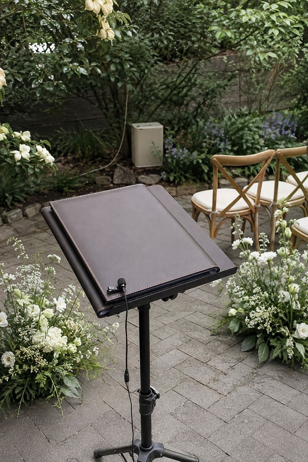 Angled logistics view connecting a tiny wireless microphone on an officiant folio with a compact neutral speaker hidden behind greenery near the back row