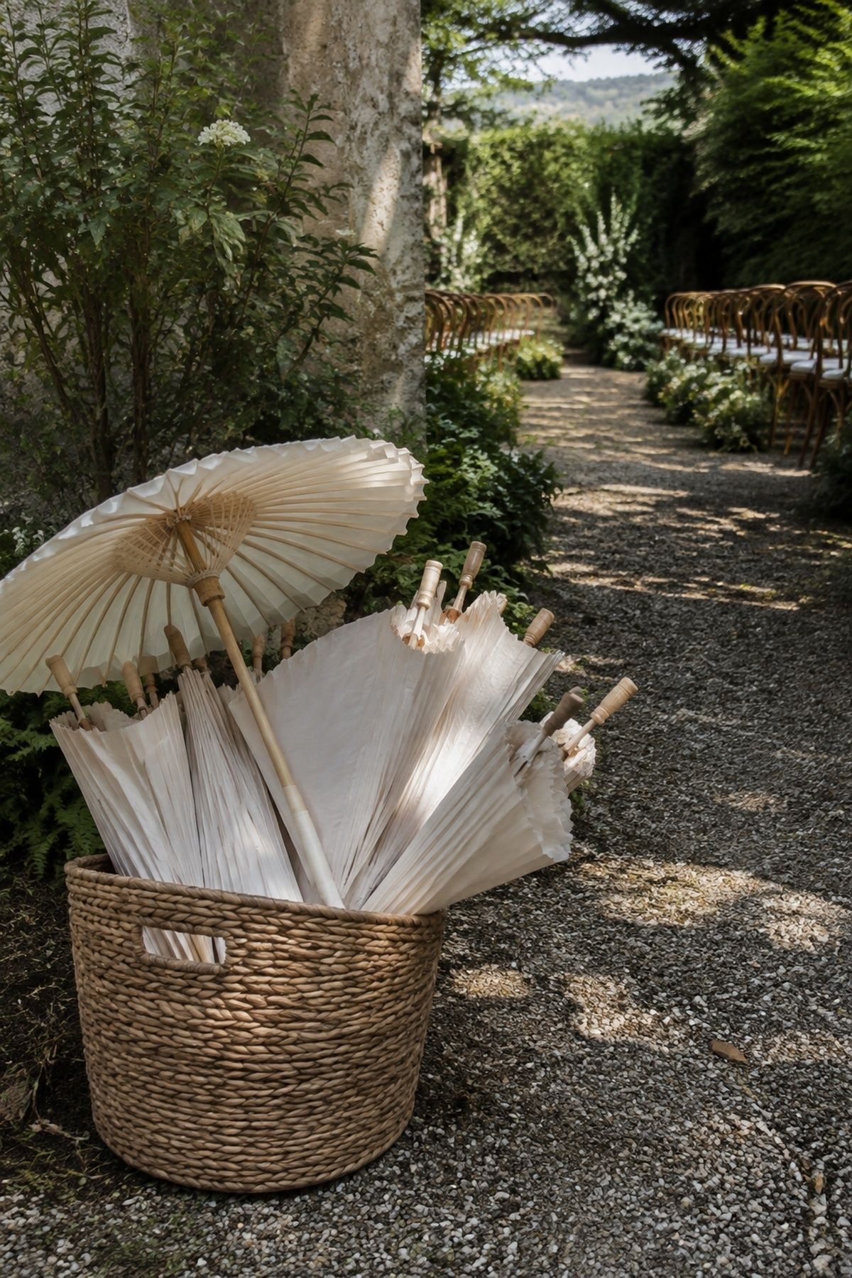 Warm white parasols in a woven basket at a shaded garden ceremony entrance
