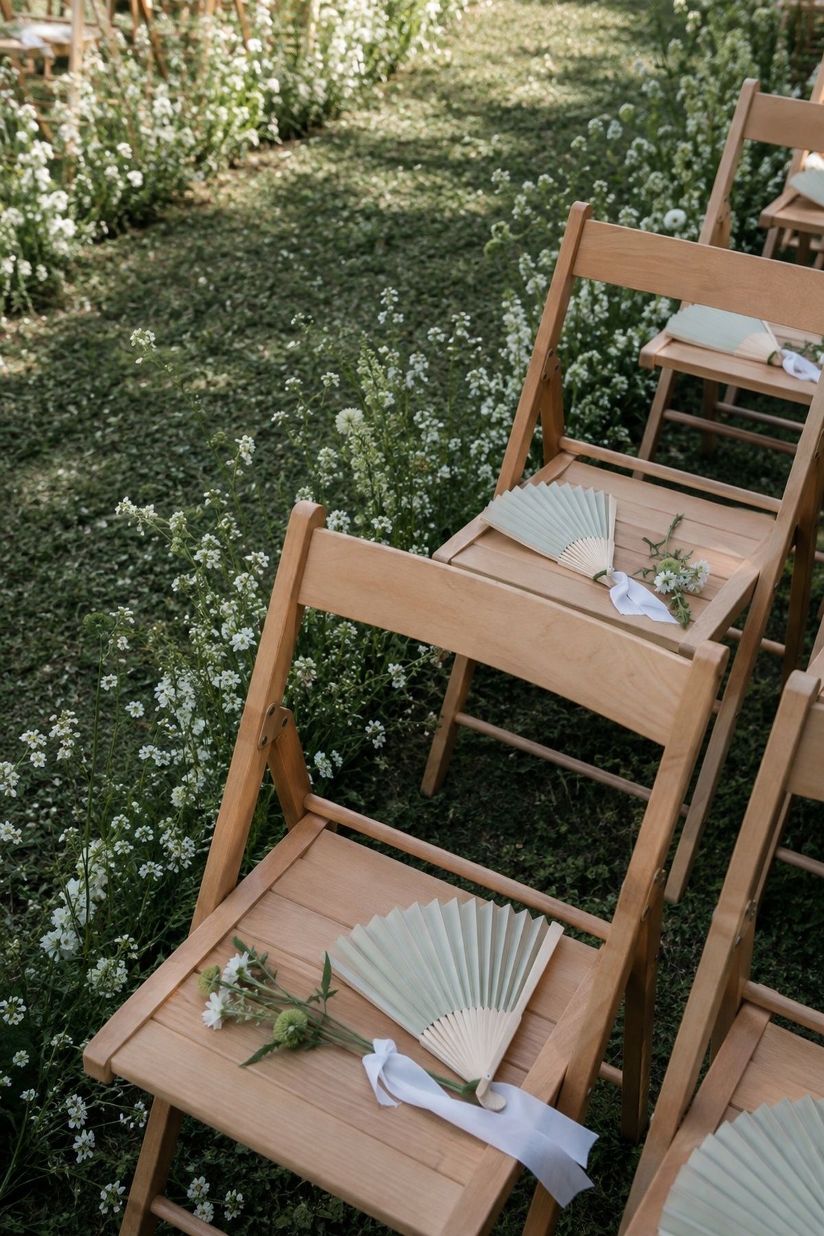 Pale sage folding program fans placed on light wood outdoor ceremony chairs