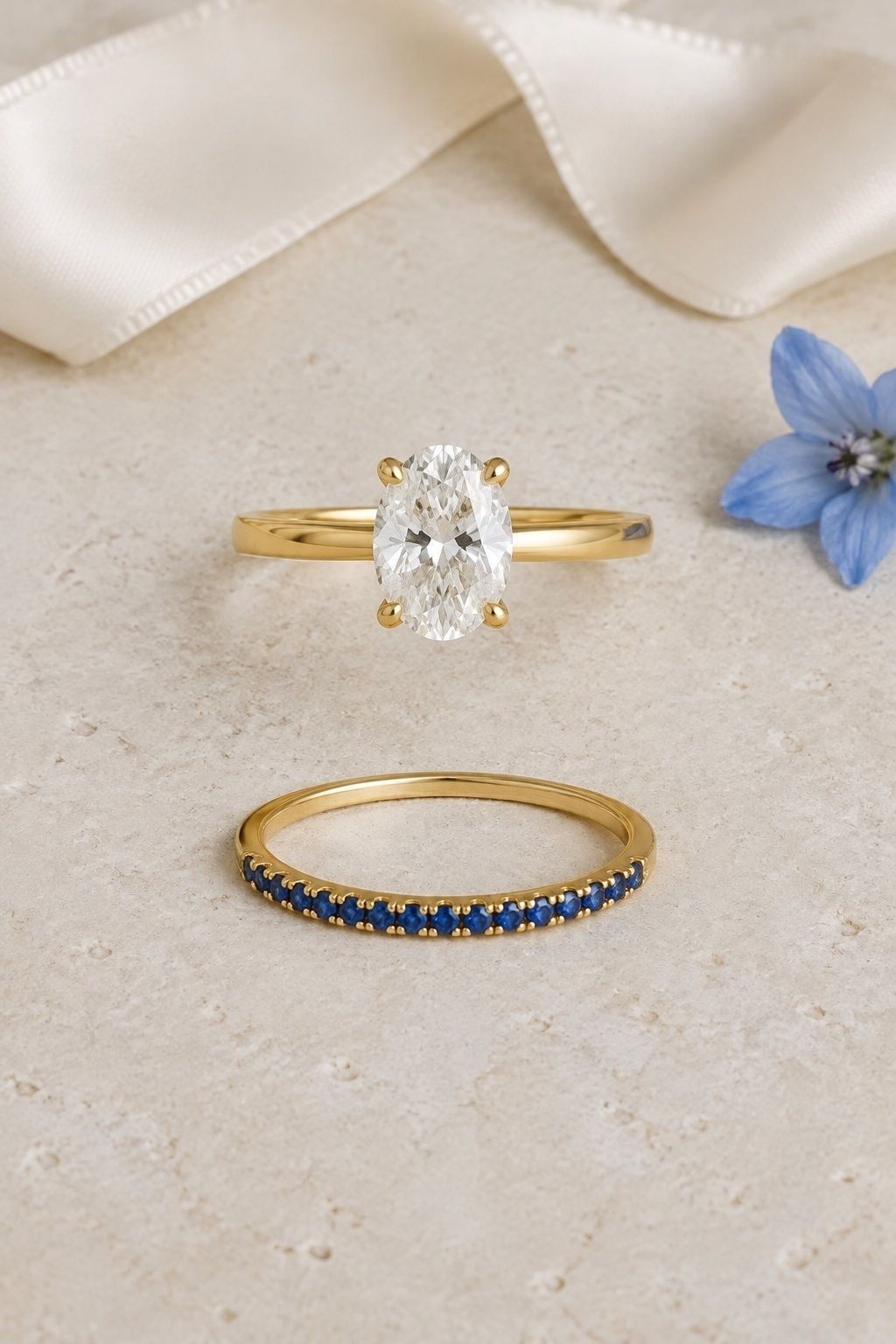 Oval engagement ring with a narrow blue sapphire wedding band on pale stone