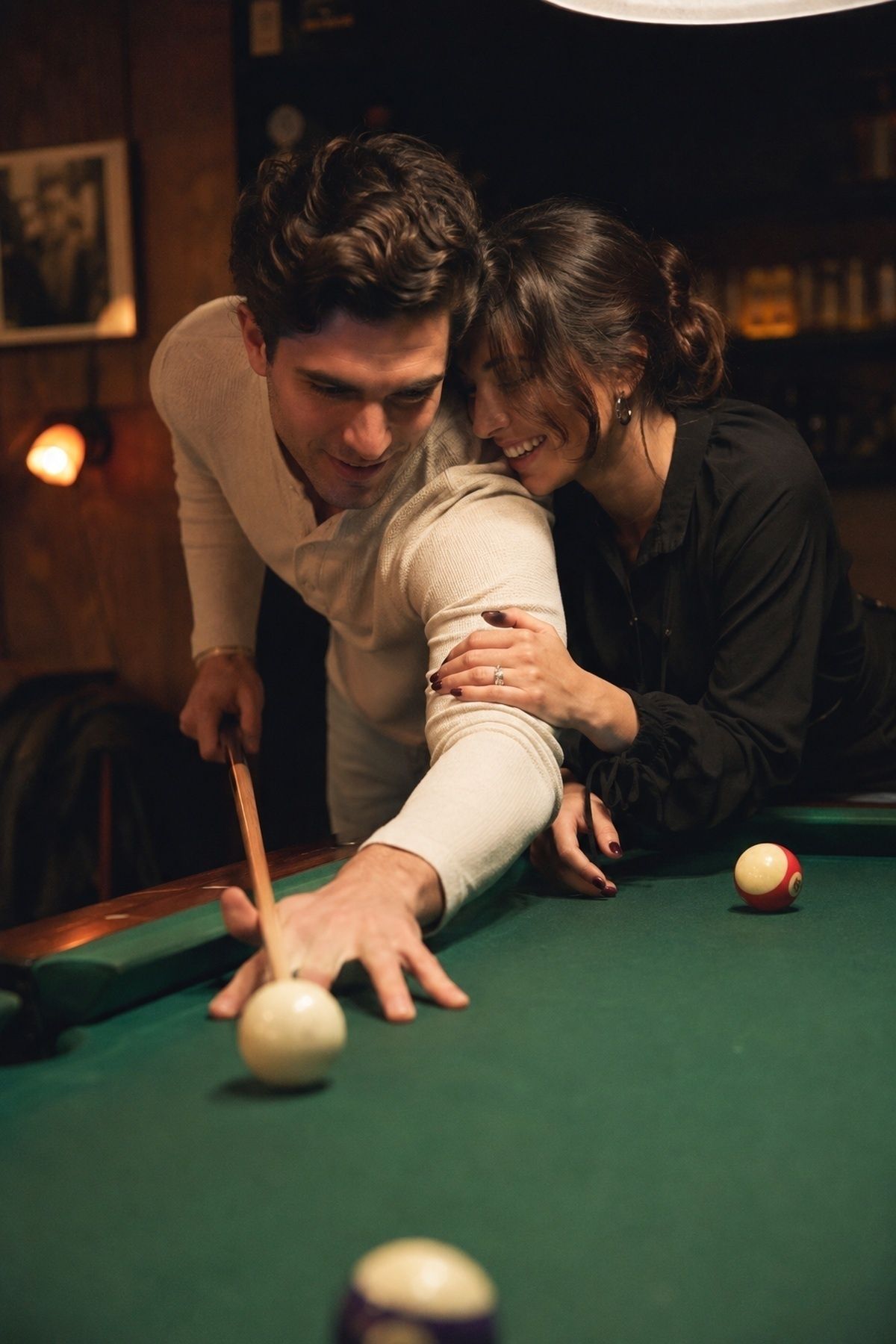 Pool table engagement couple leaning over the table together while lining up a shot