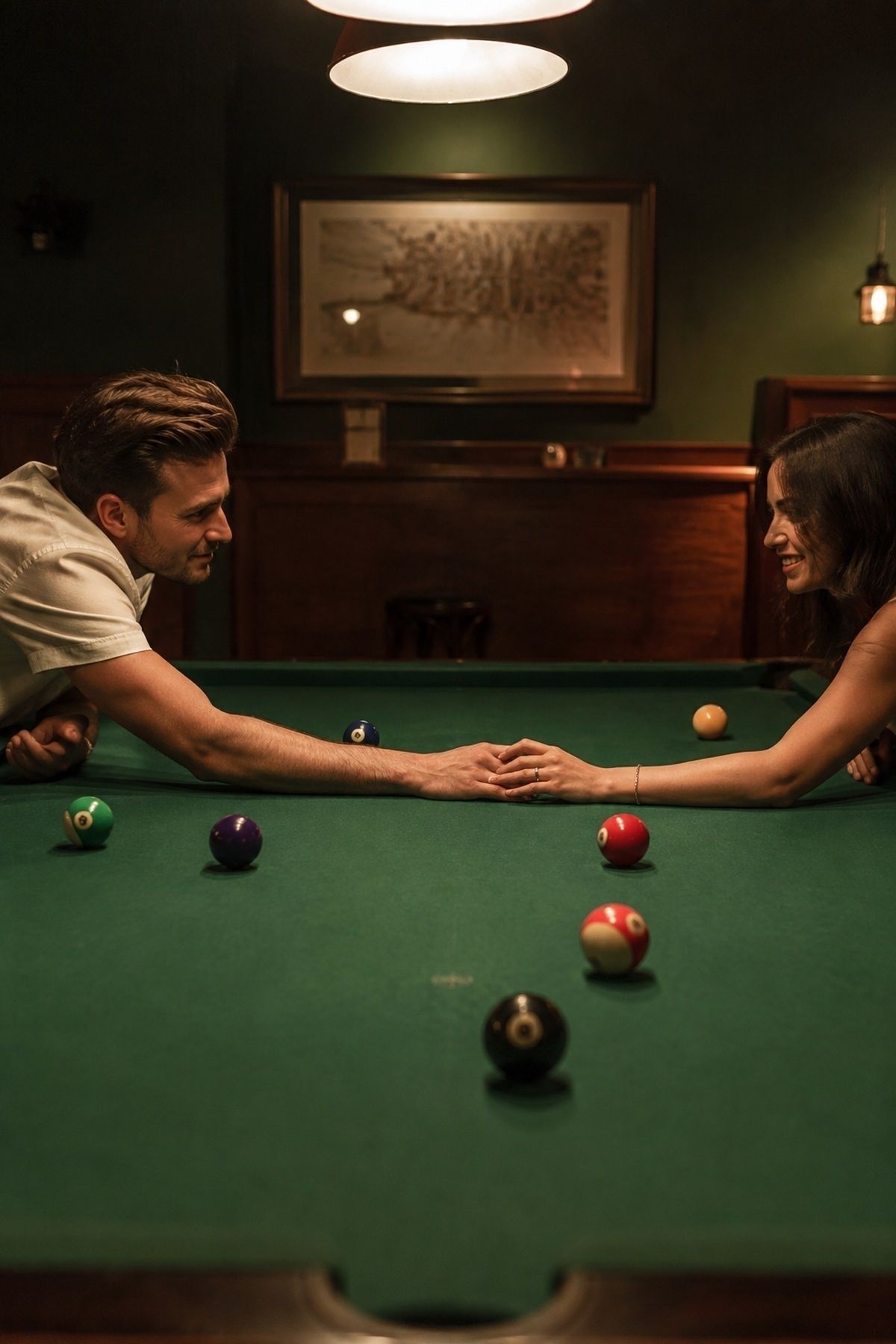Pool hall engagement couple reaching across a green pool table with clean leading lines